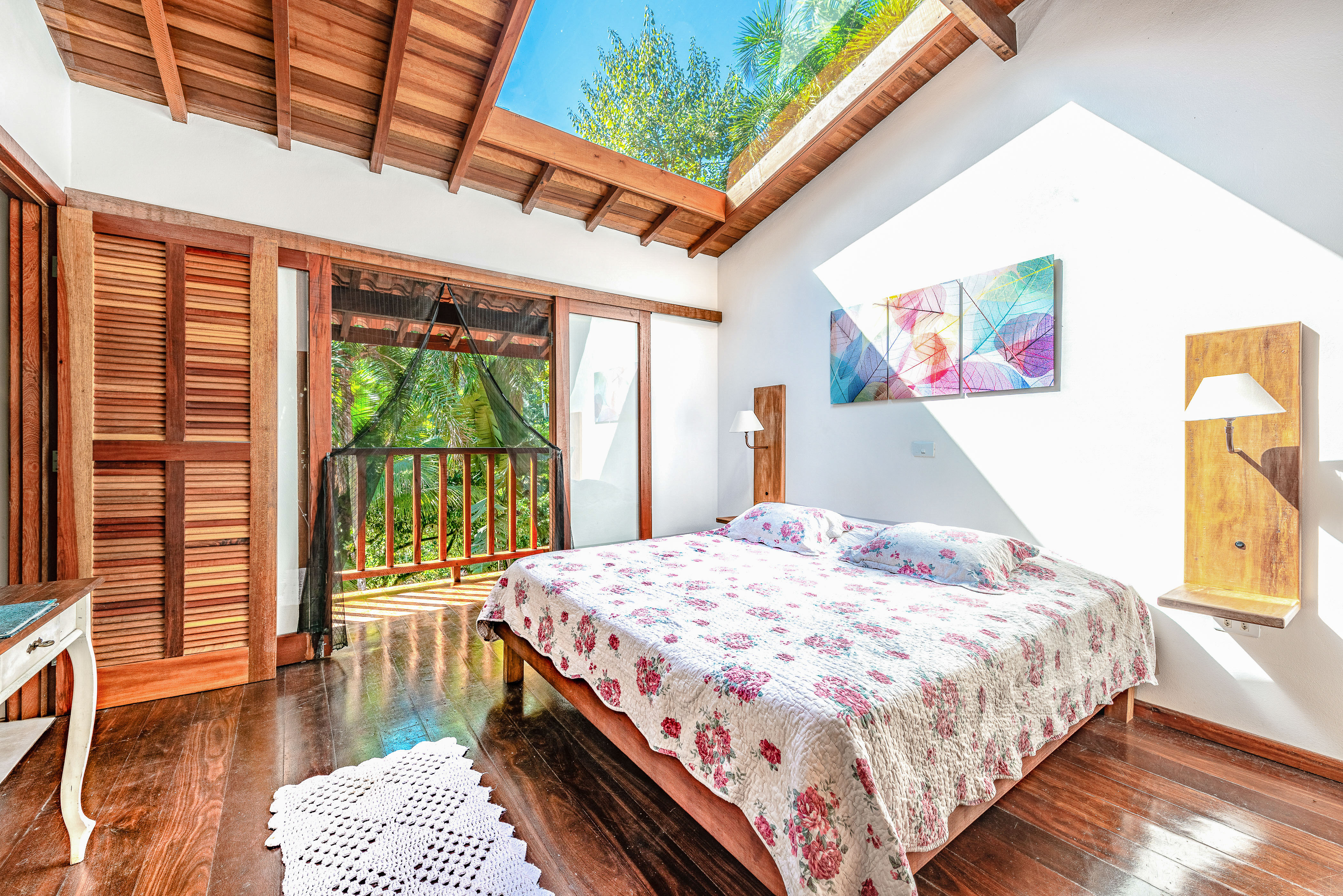Bright bedroom with floral bedspread and wood paneled ceilings lit by a skylight and open terrace door.