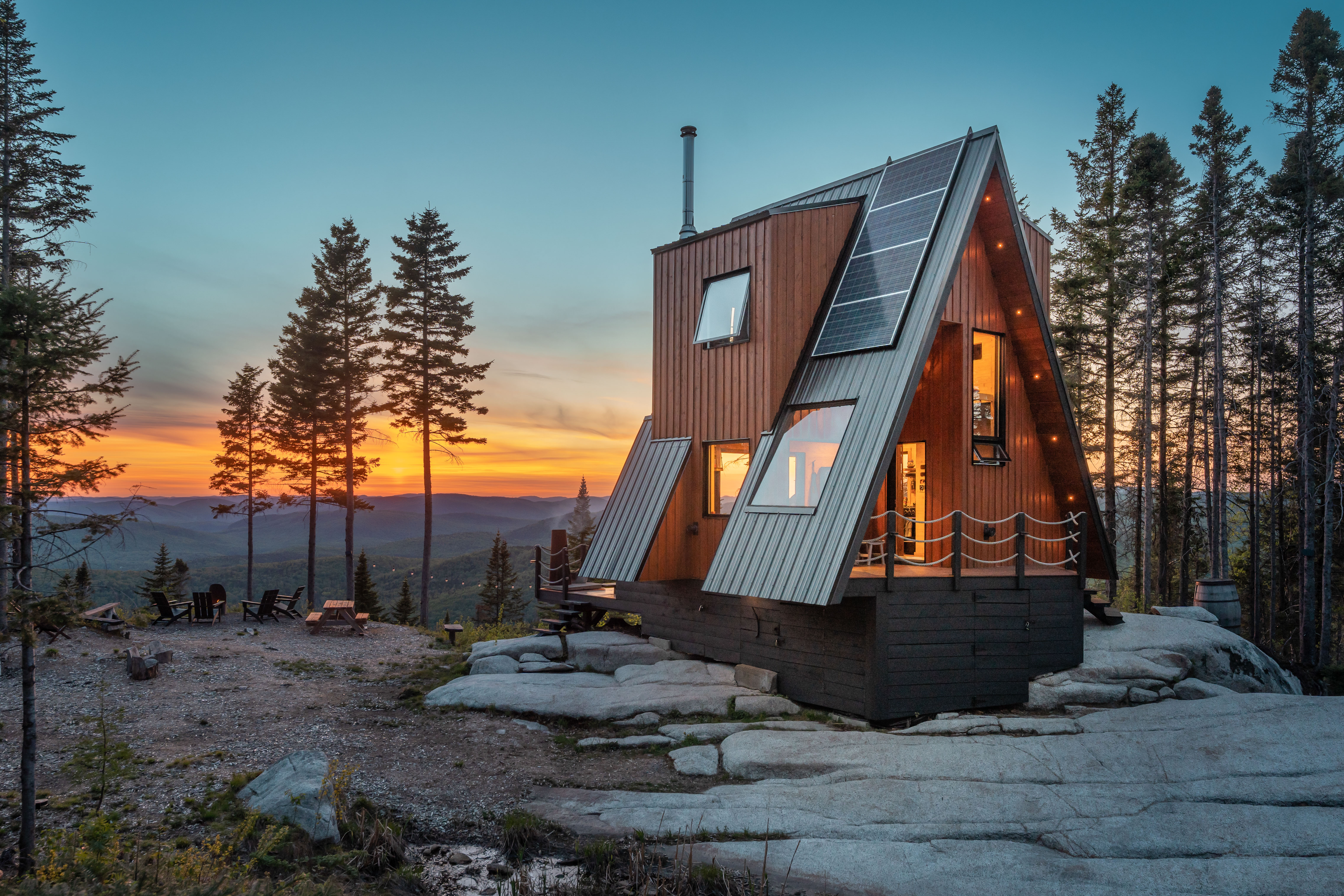 Elevated A-frame cabin lit from the inside atop a mountain overlook at sunset.