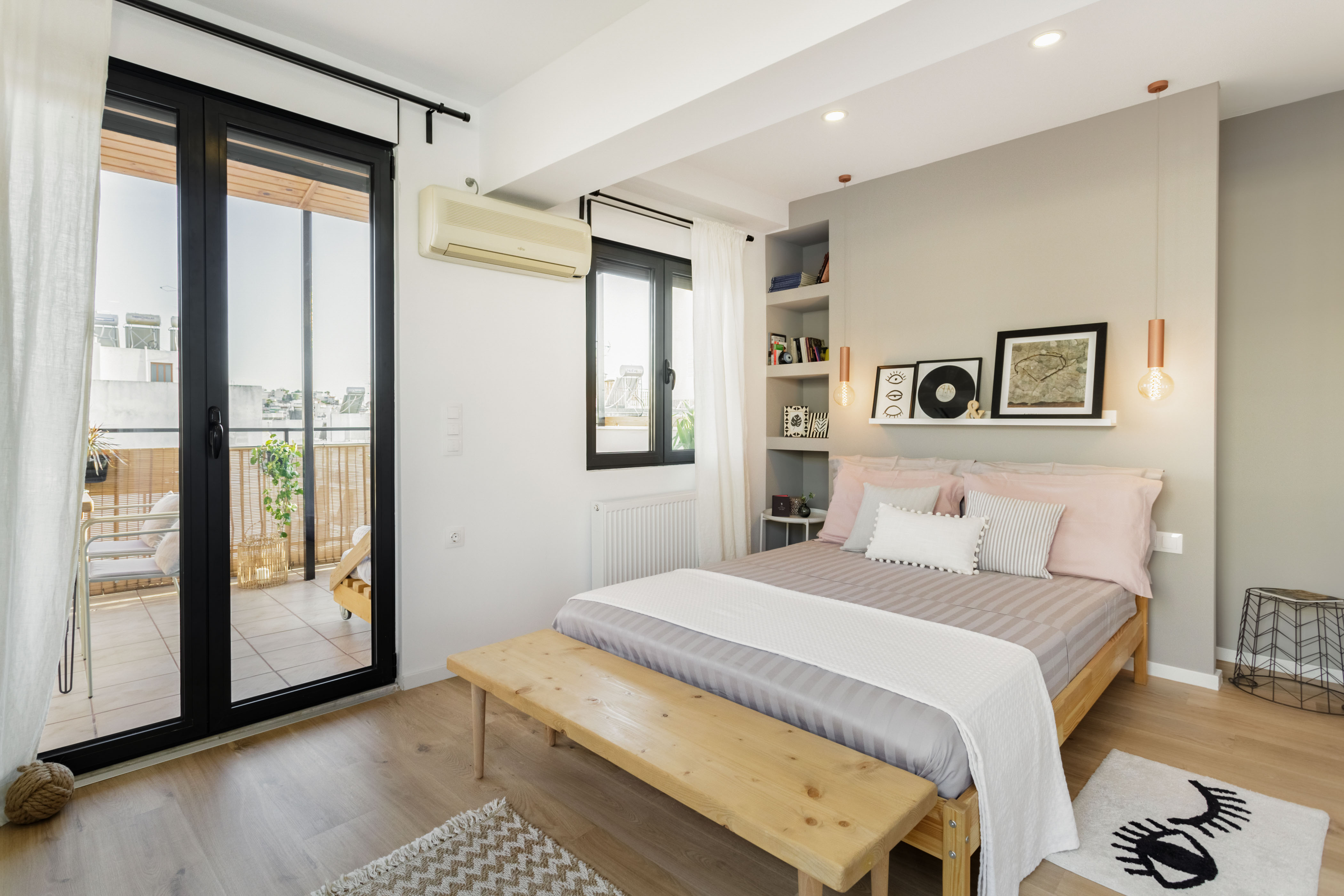Bedroom with grey walls and light wooden frame near a glass door that leads out to a sunny terrace.