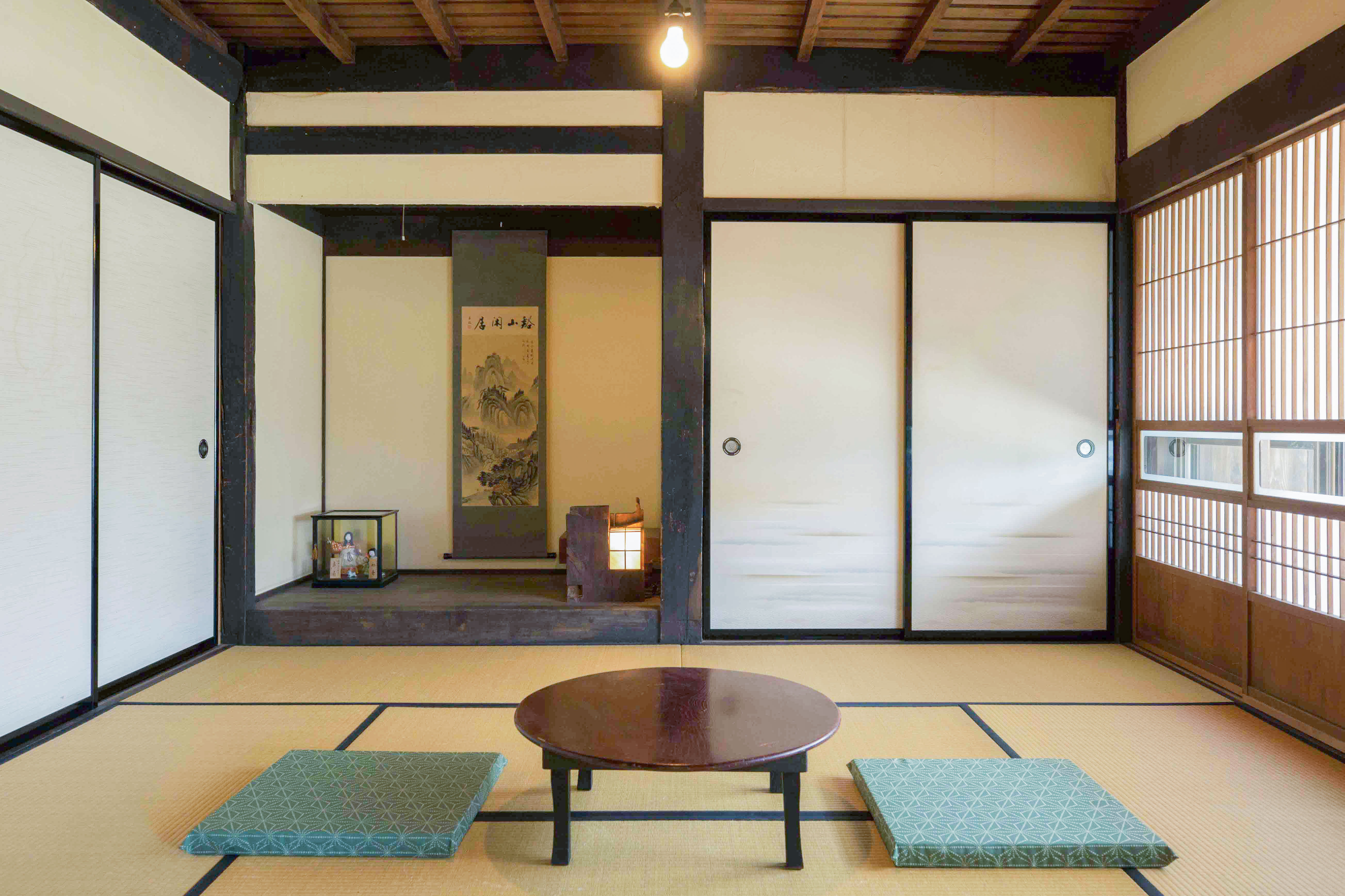Japanese style room with two cushions and a low, round table, leading to a wooden hallway lightly decorated.