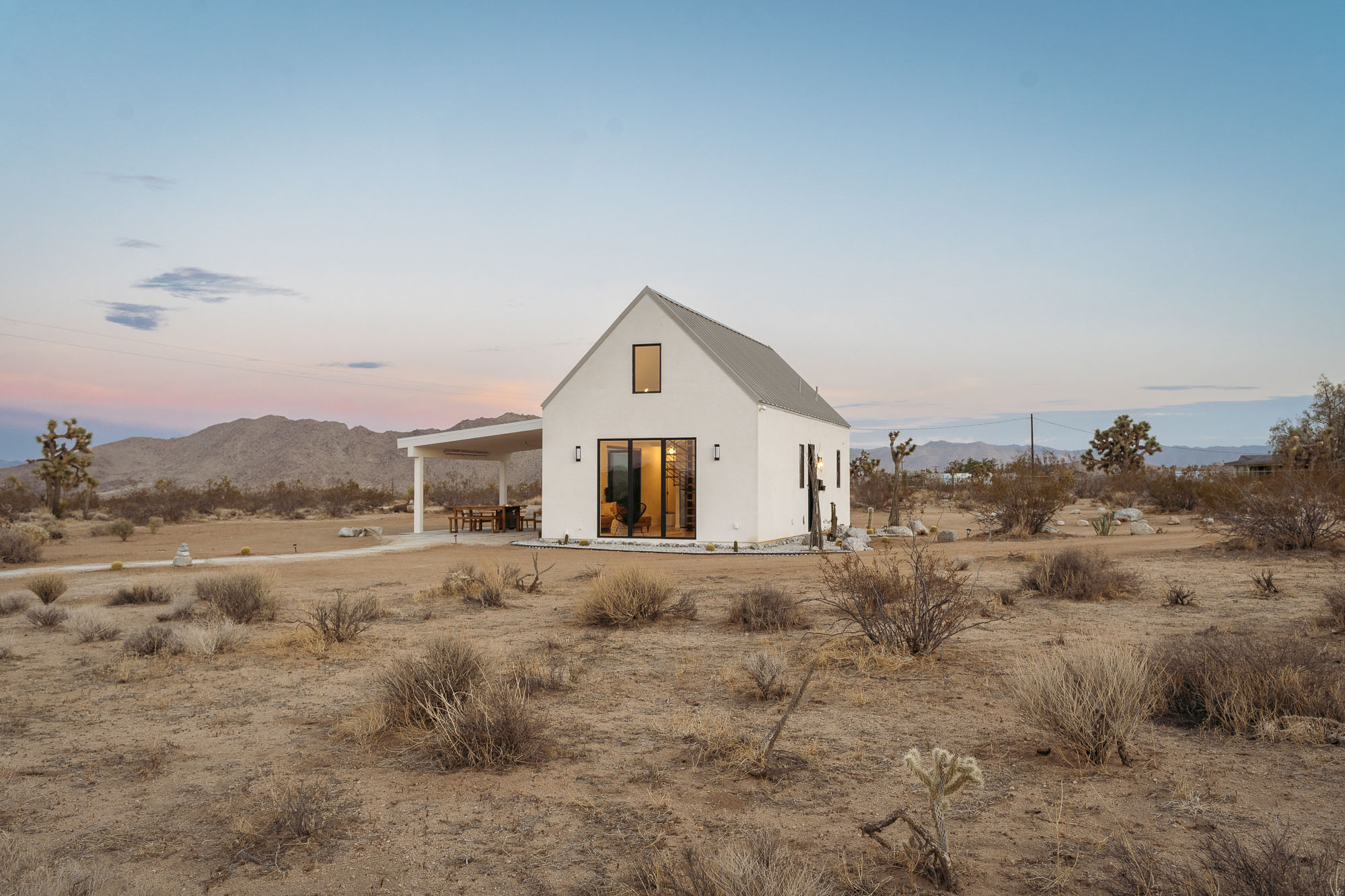 White house with overhang porch in a desert landscape.