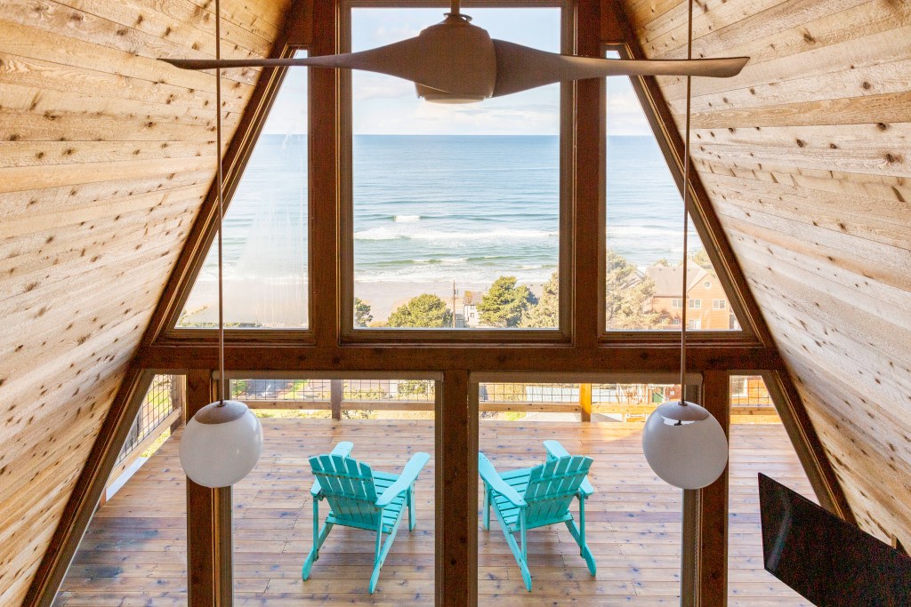 View of the deck inside a timber A-Fram cabin, looking out to the ocean. 