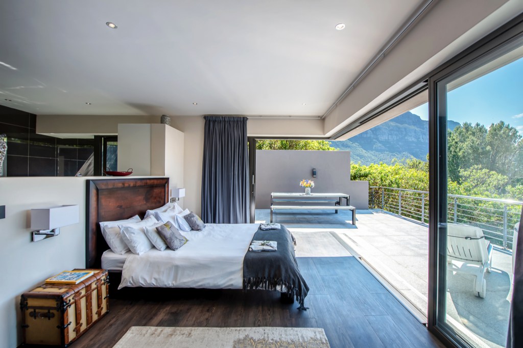 Picture of a king size bed, with windows opening up to a balcony and a view of surrounding mountains. 