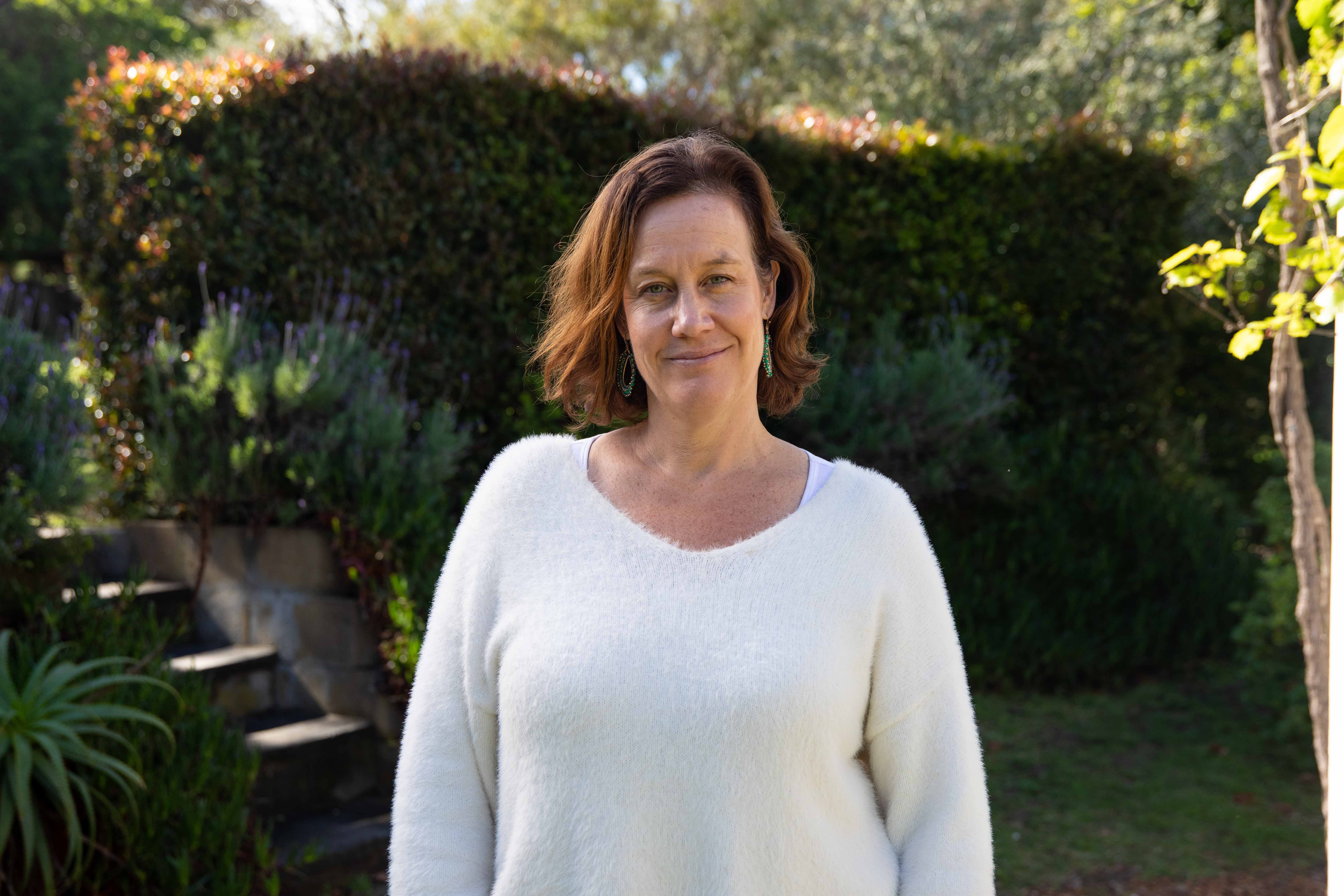 A woman in a white sweater with short brown hair standing outdoors. 