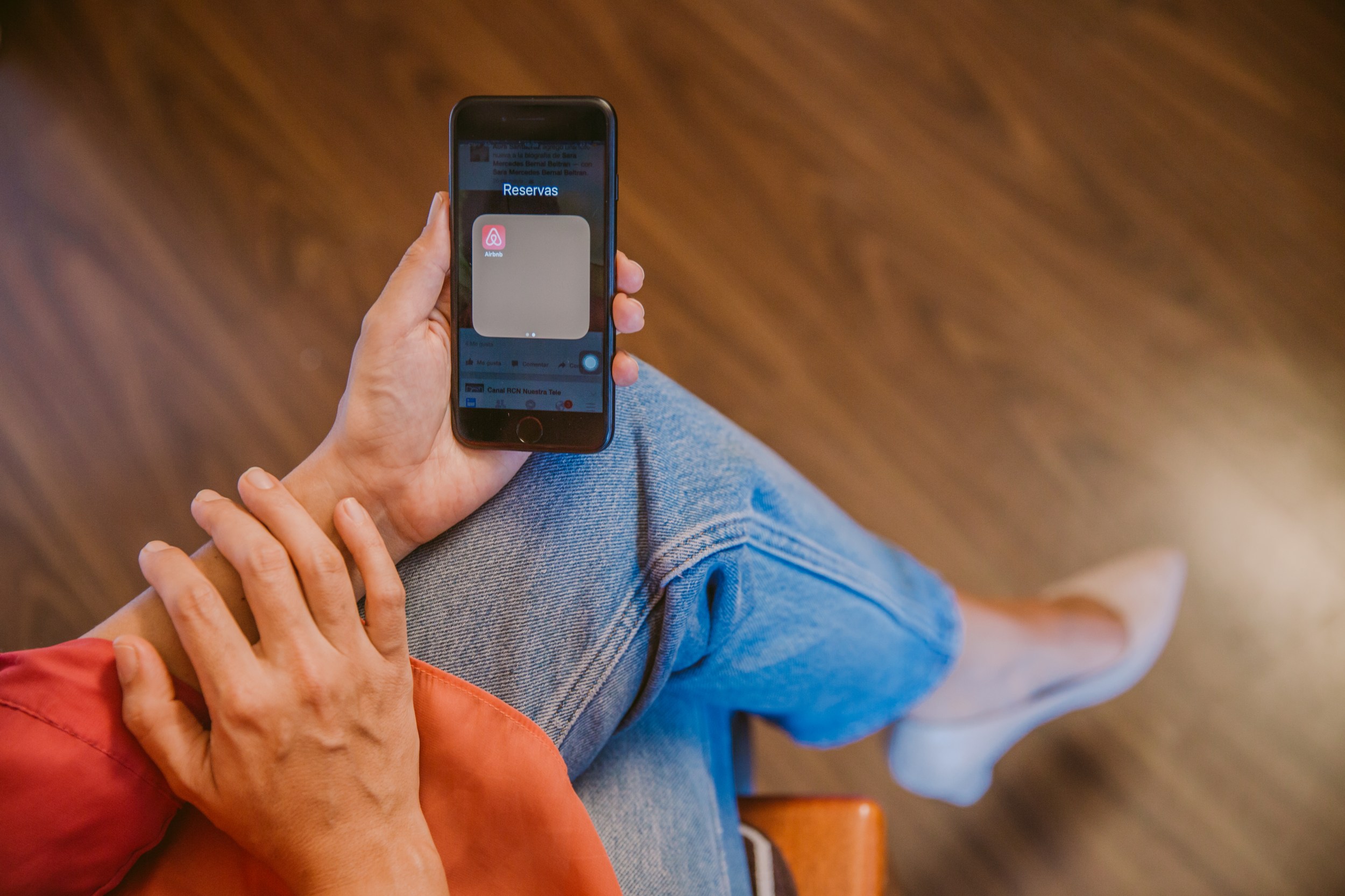 Booking Mujer sostiene su celular y se ve la aplicacion de Airbnb en la pantalla