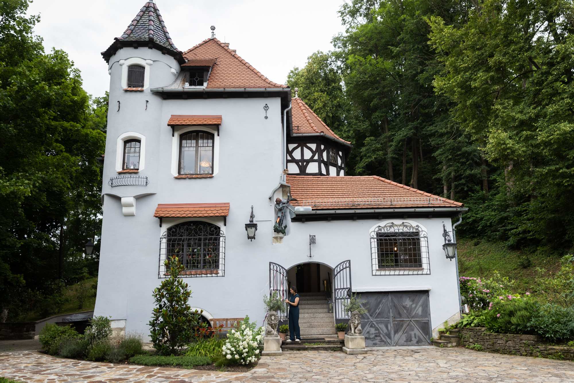 The historical home is embedded in a dark green forest with a small tower and many roof shingles. 