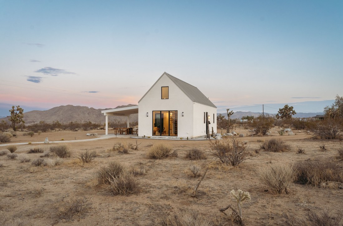White house with an overhang porch in a desert landscape.