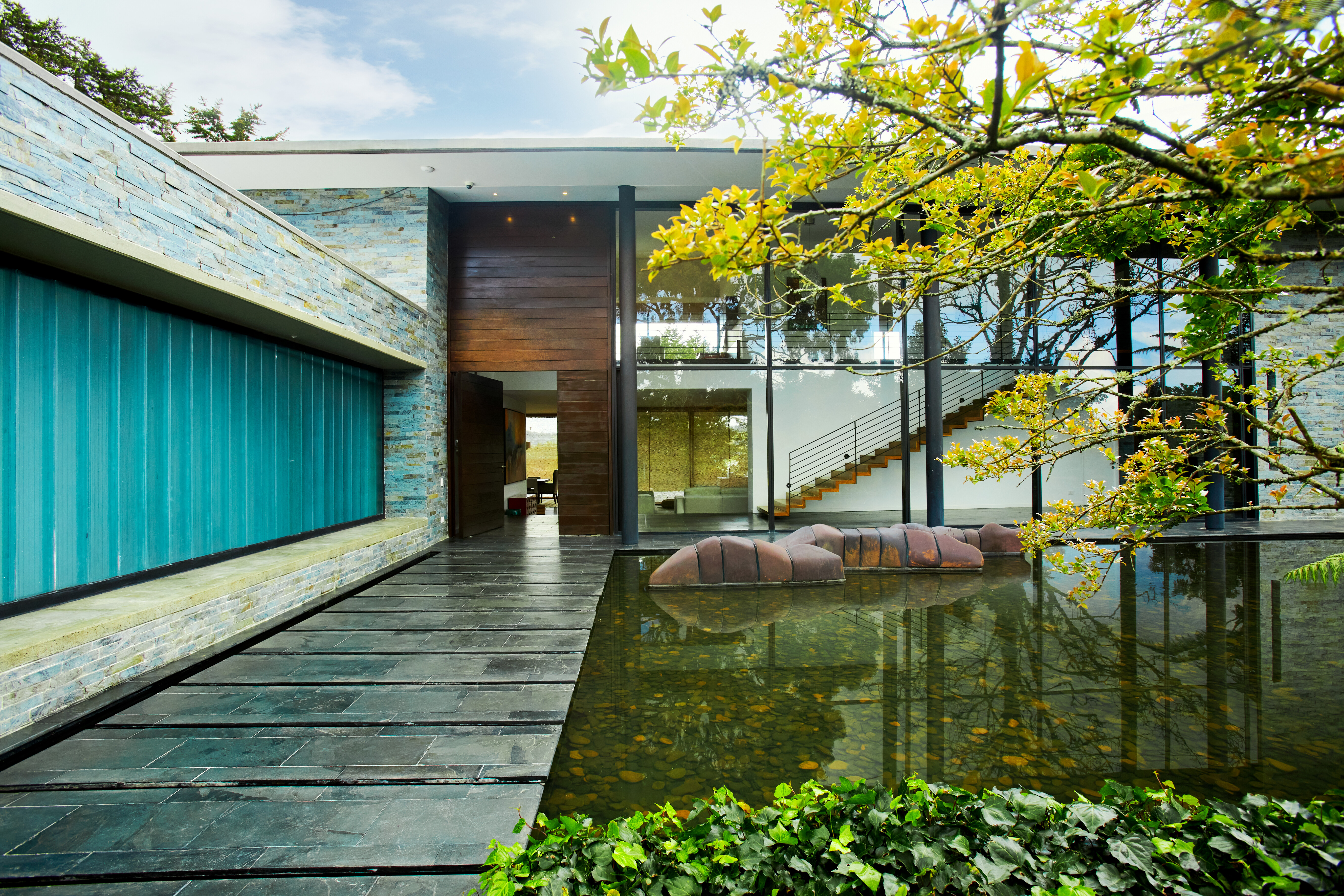 Front shot of Colombian artist JUANES in Envigado, Colombia. Front wide shot of the house with a path that leads to an open door. Trees in the right and blue toned window in the left