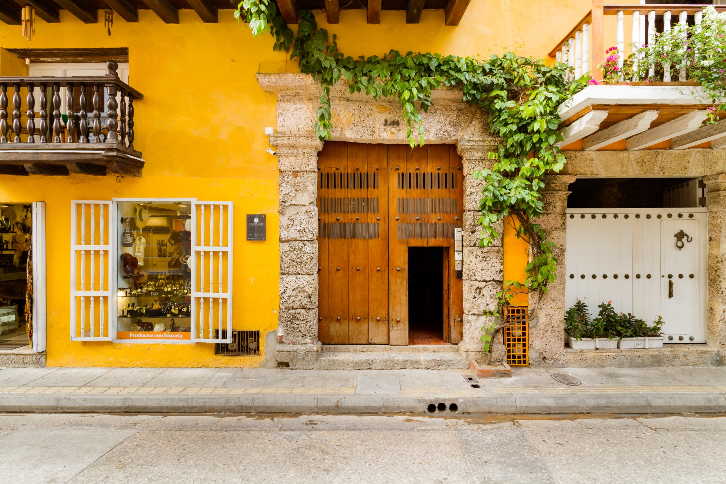 Exterior frontal de una casa colonial amarilla en Cartagena, Colombia. Con puerta de madera a la derecha y una enredadera encima de la puerta.