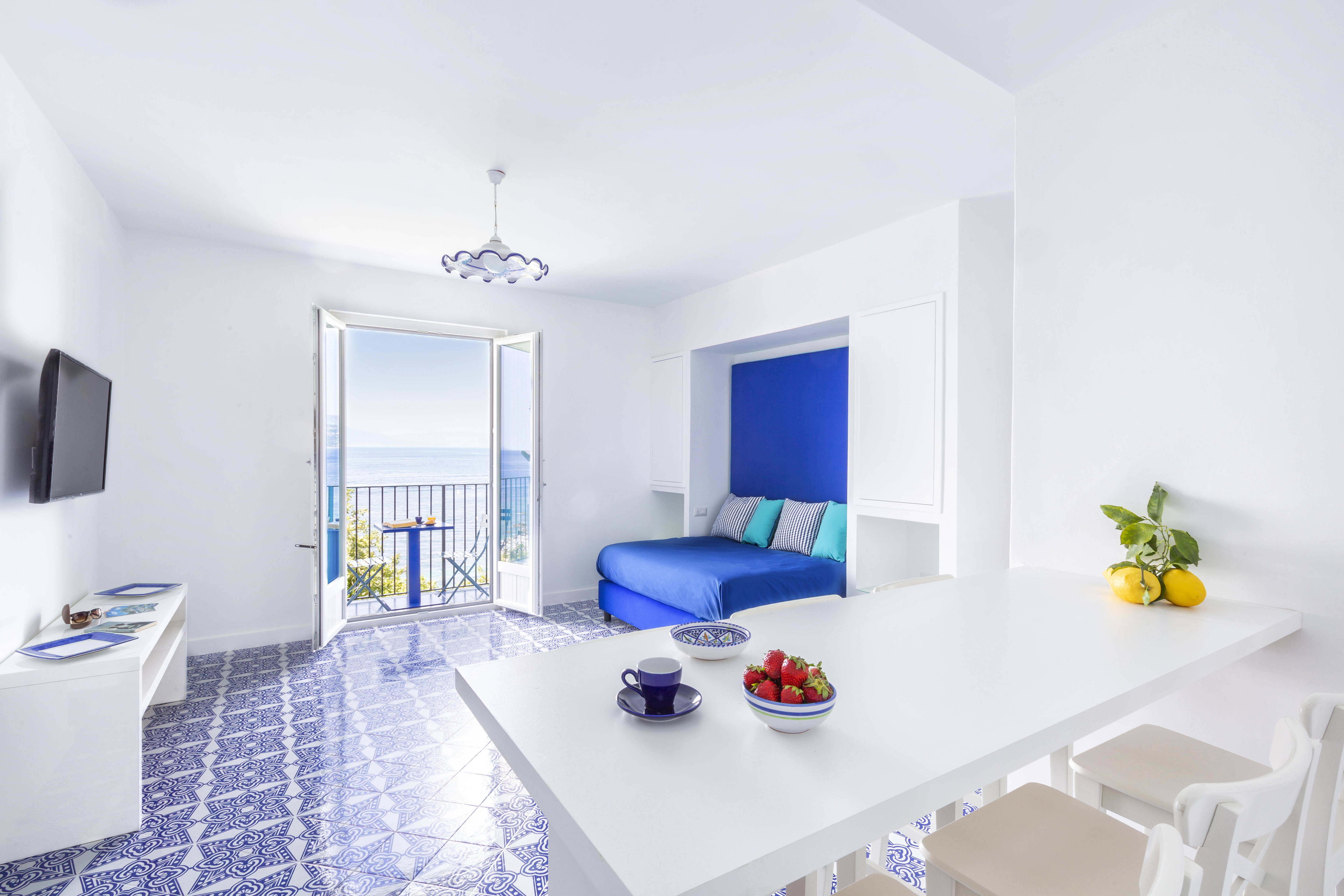 A white room with a blue murphy bed and blue tiled floor and a white high top table with seating.