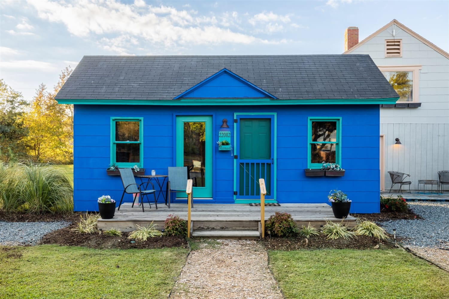 A bright blue tiny home with turqouise trim and a small front porch and flower planters out front.