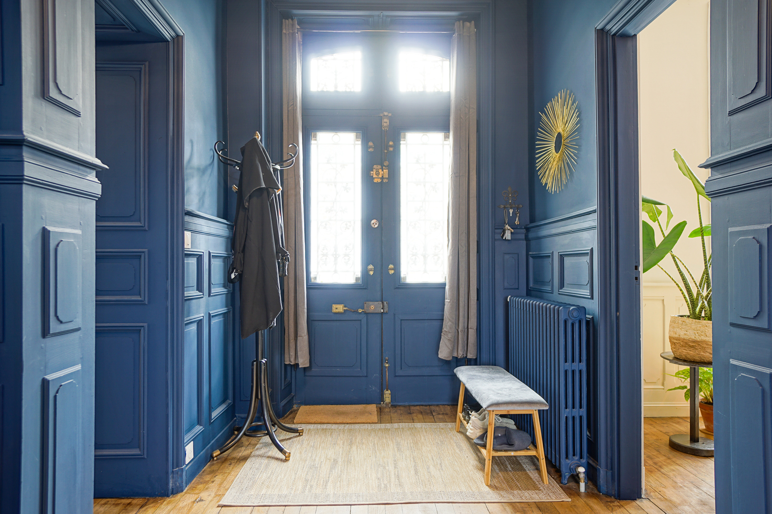 A blue entryway with double doors and a gold mirror and resting bench.