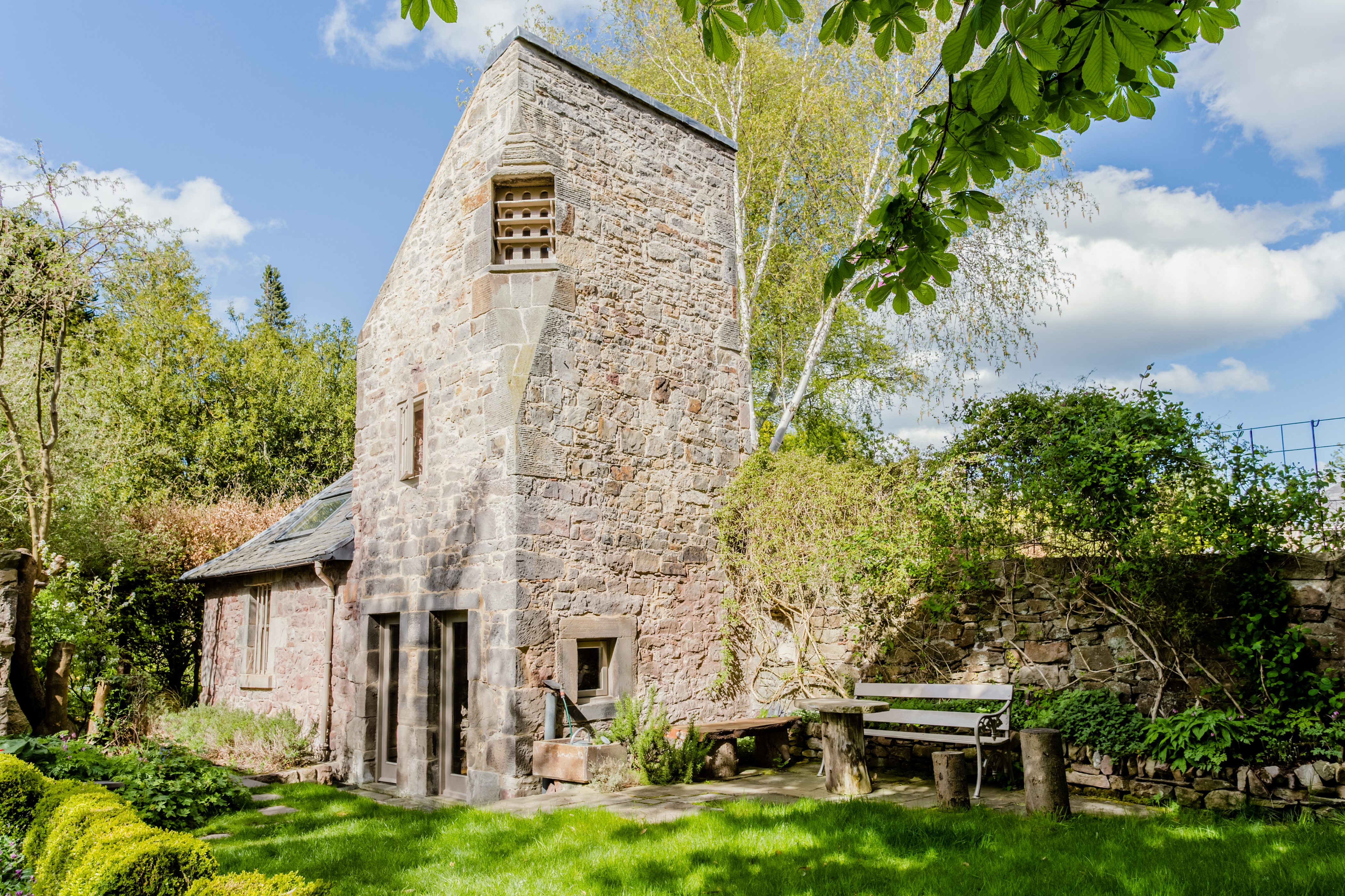 Exterior shot of a small and slender stone dovecot set on a lush green lawn in an Edinburgh garden.