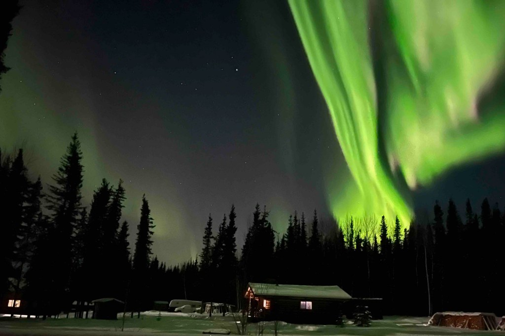 Green northern lights shooting up behind a dimly lit home. 