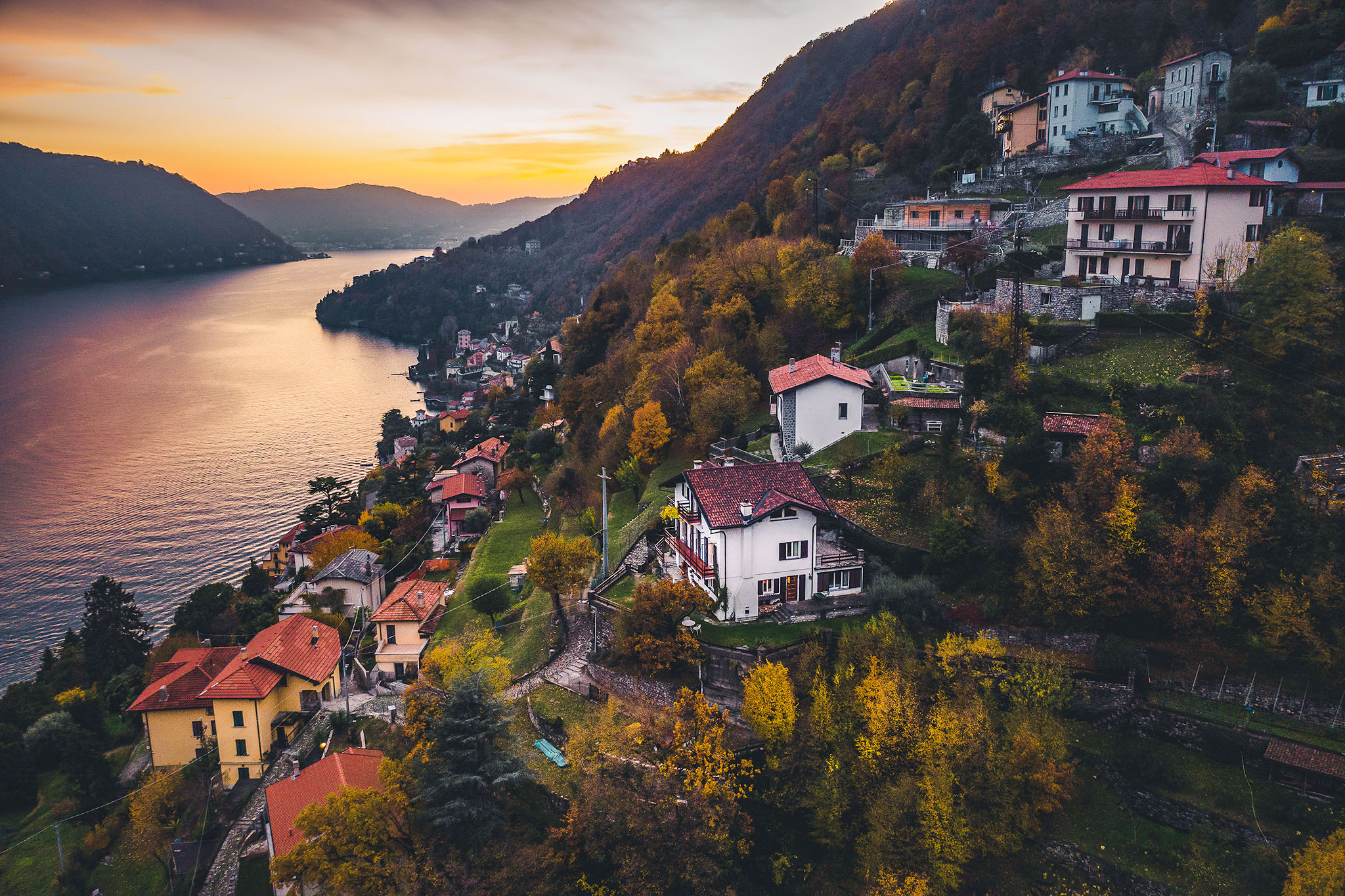 Ariel shot of a three story-white villa overlooking Lake Como at sunset.