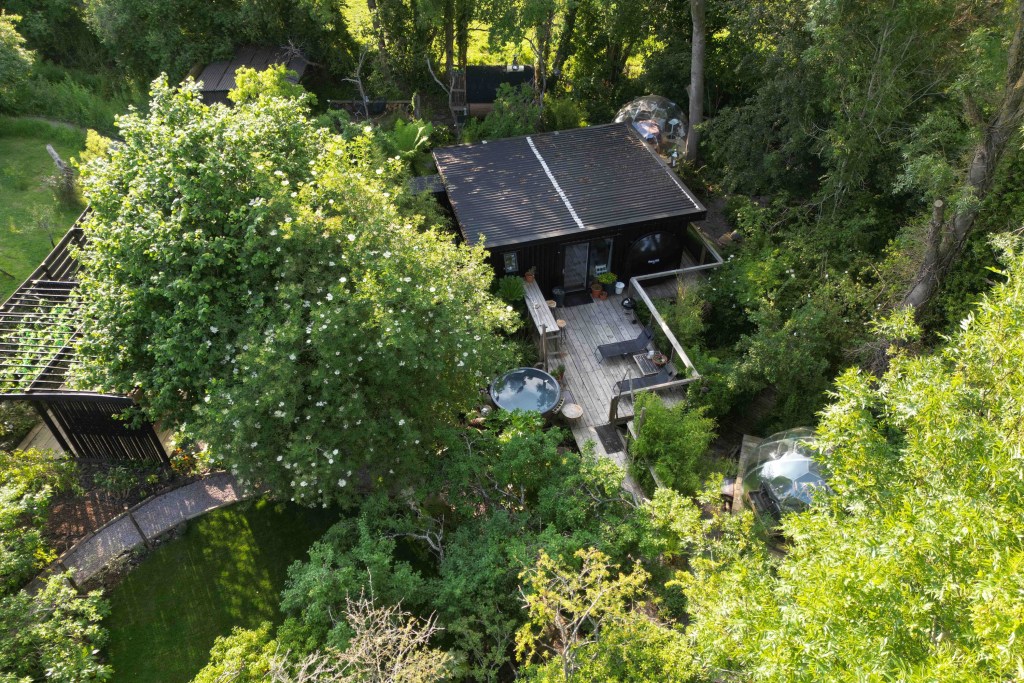 Ariel shot of a timber clad flat roofed cabin nestled in a grove in Worcestershire, England.