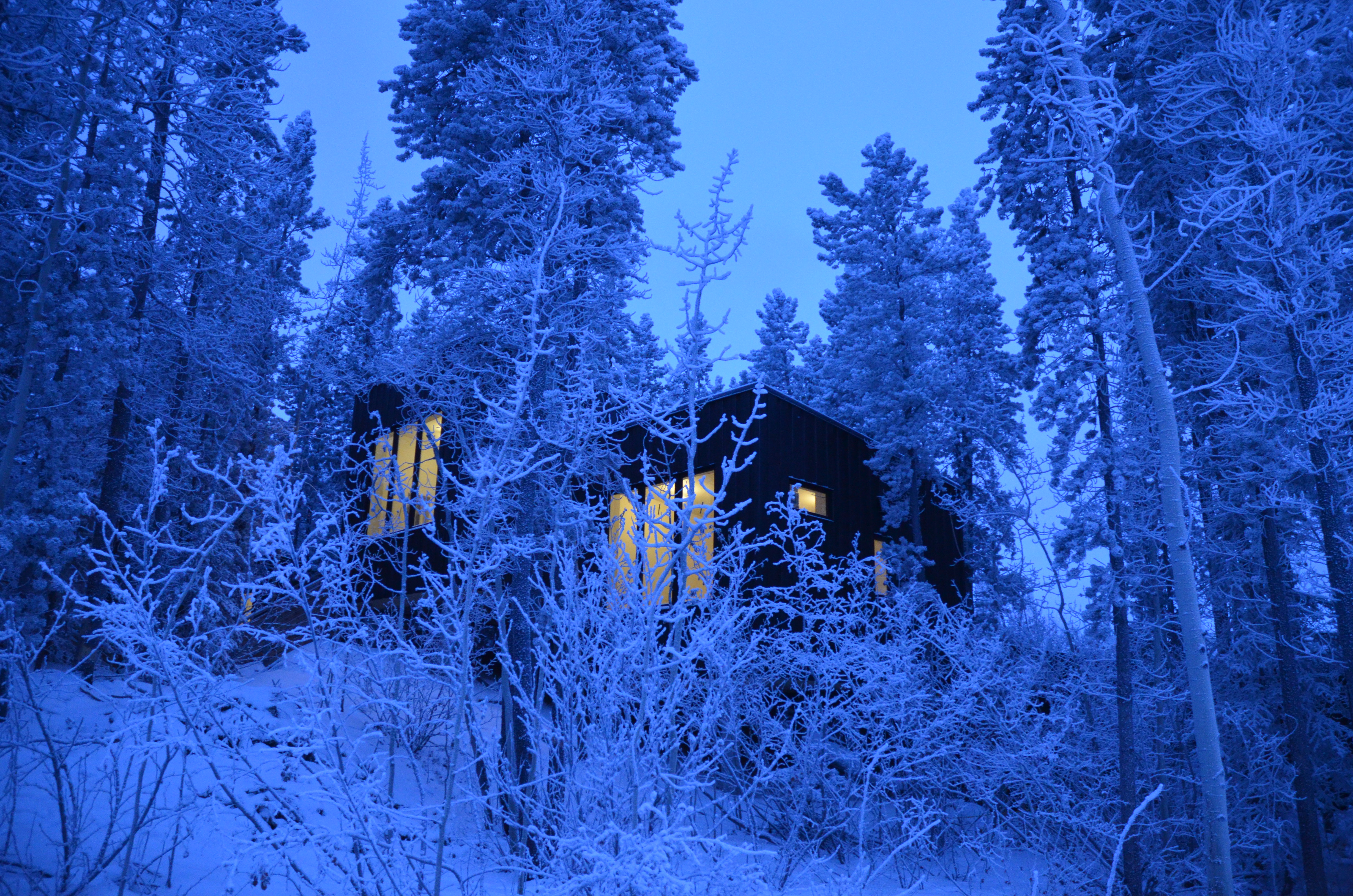 A cabin at twilight in the winter surrounded by snow-capped trees