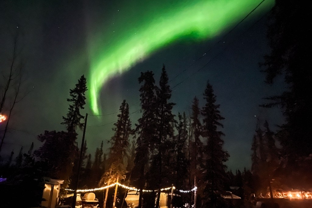 Northern Lights above a circle of chairs around a firepit
