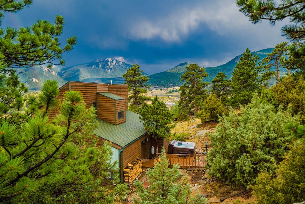 Exterior shot of a timberclad dormer house with mountains in the background. Hot tub and decking also visible in the shot.