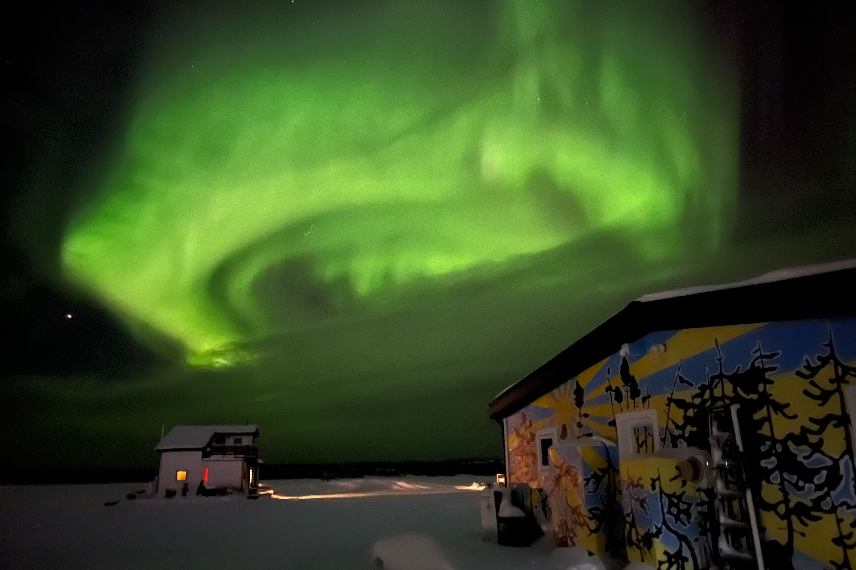 Green Northern Lights swirl above a houseboat.