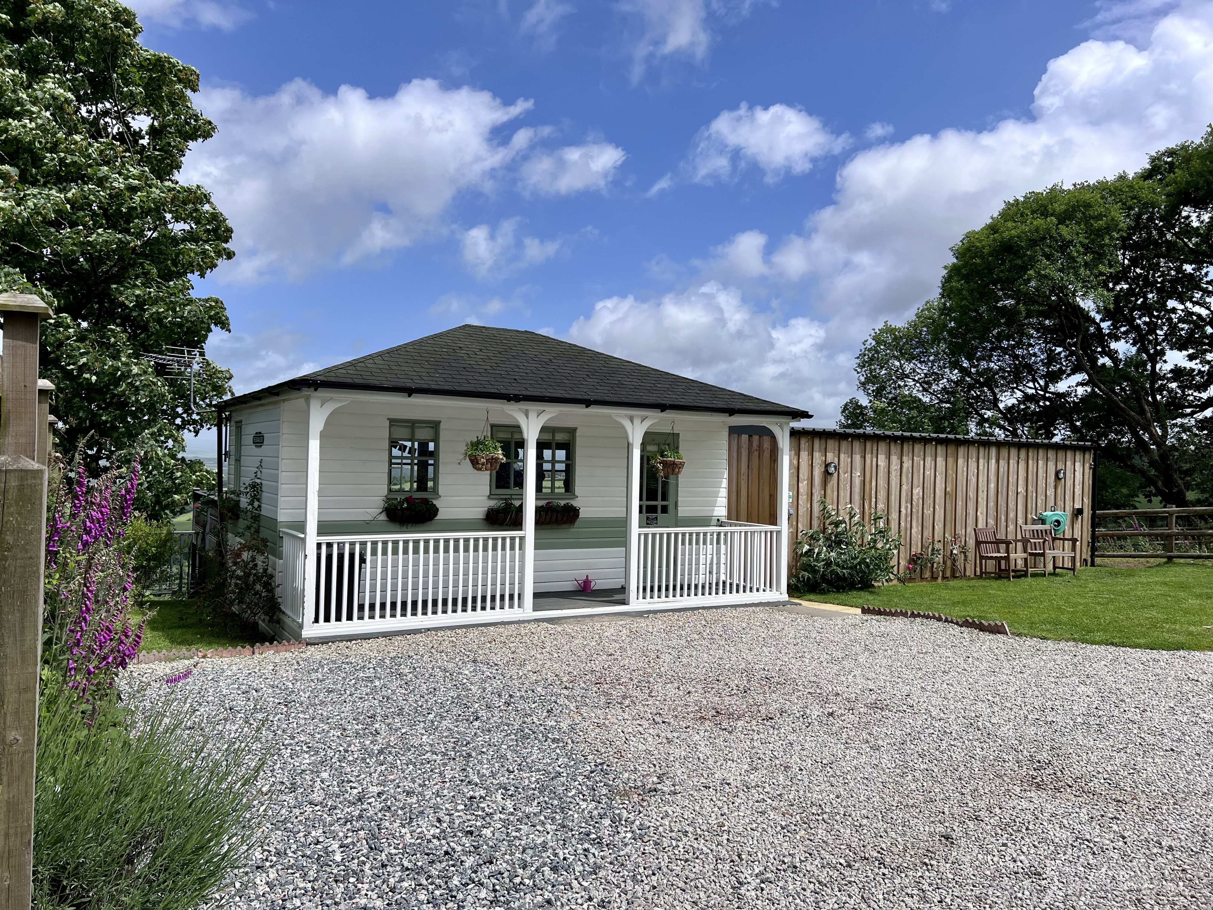 Exterior shot of a timber clad white cabin in Cornwall. Gravel driveway and lawn in the foreground.