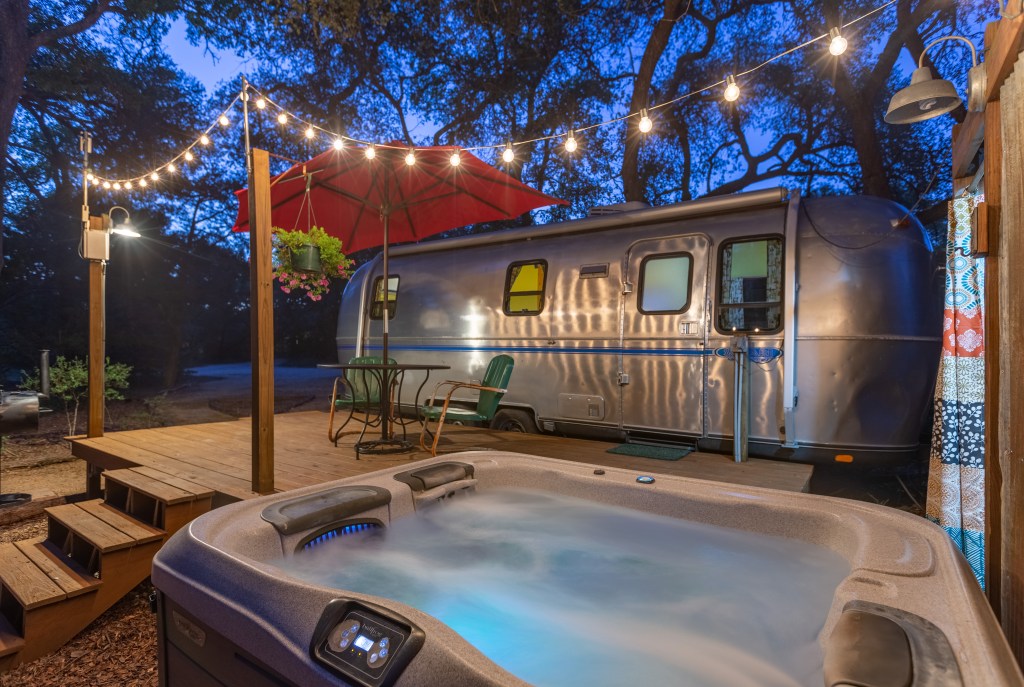 Exterior shot of a chrome airstream trailer featuring a hot tub in the foreground.