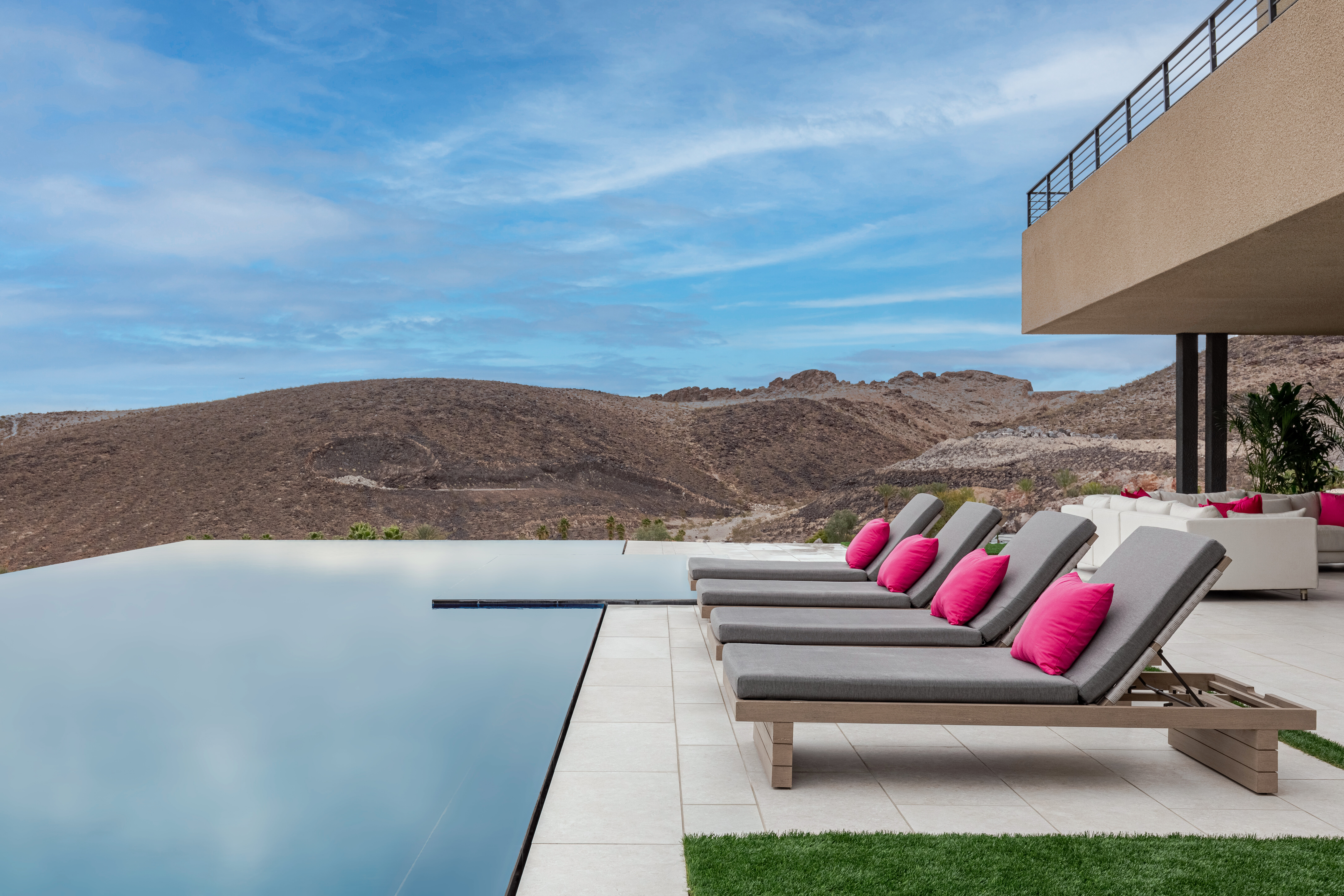 Outdoor pool featuring lounge chairs and couches with pink pillows looking out to the Las Vegas desert.
