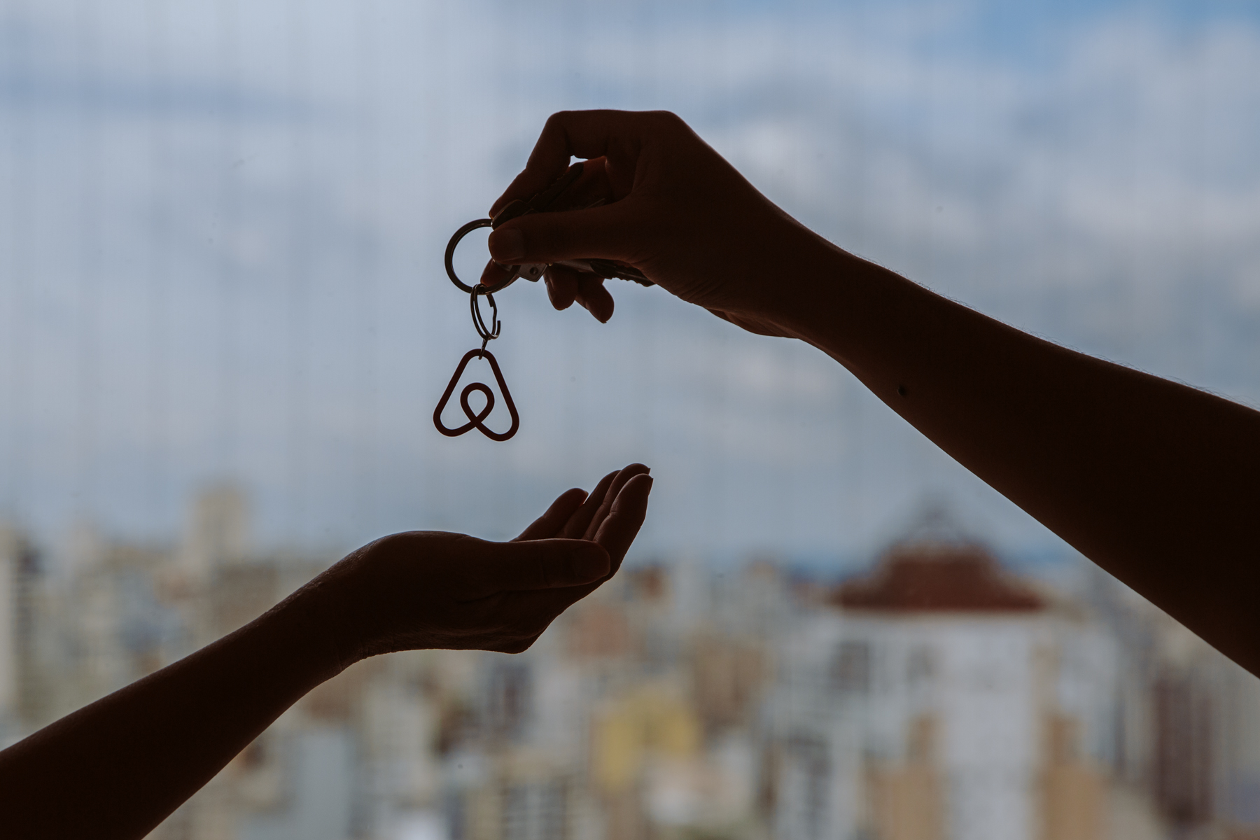 Una mano entrega a otra unas llaves con llavero de logo de Airbnb