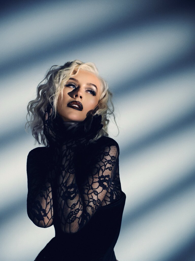 Christina Aguilera in black, looking dramatically to the right with beams of light shining on her.