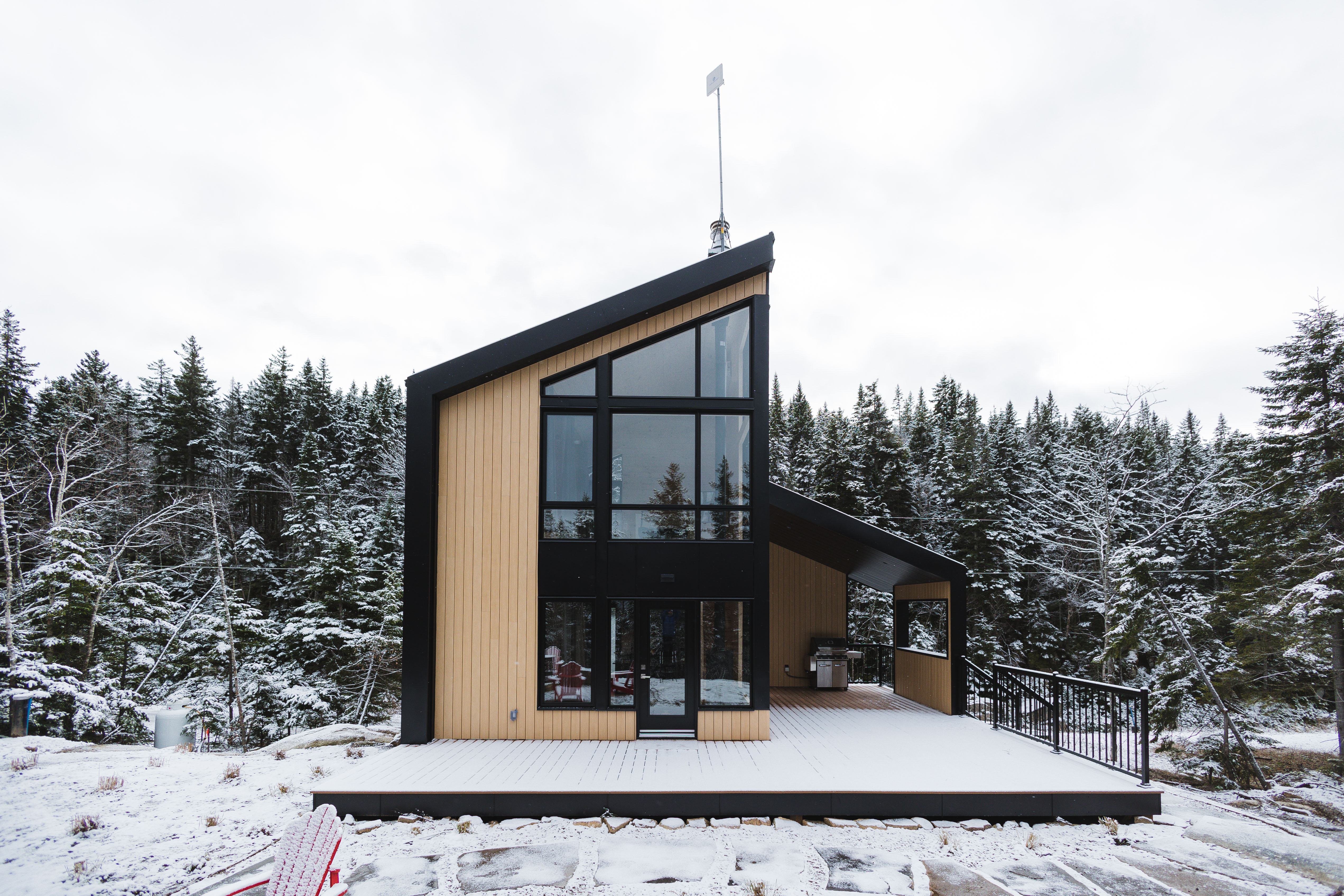 A tiny home with a deck surrounded by forestry in snow. 