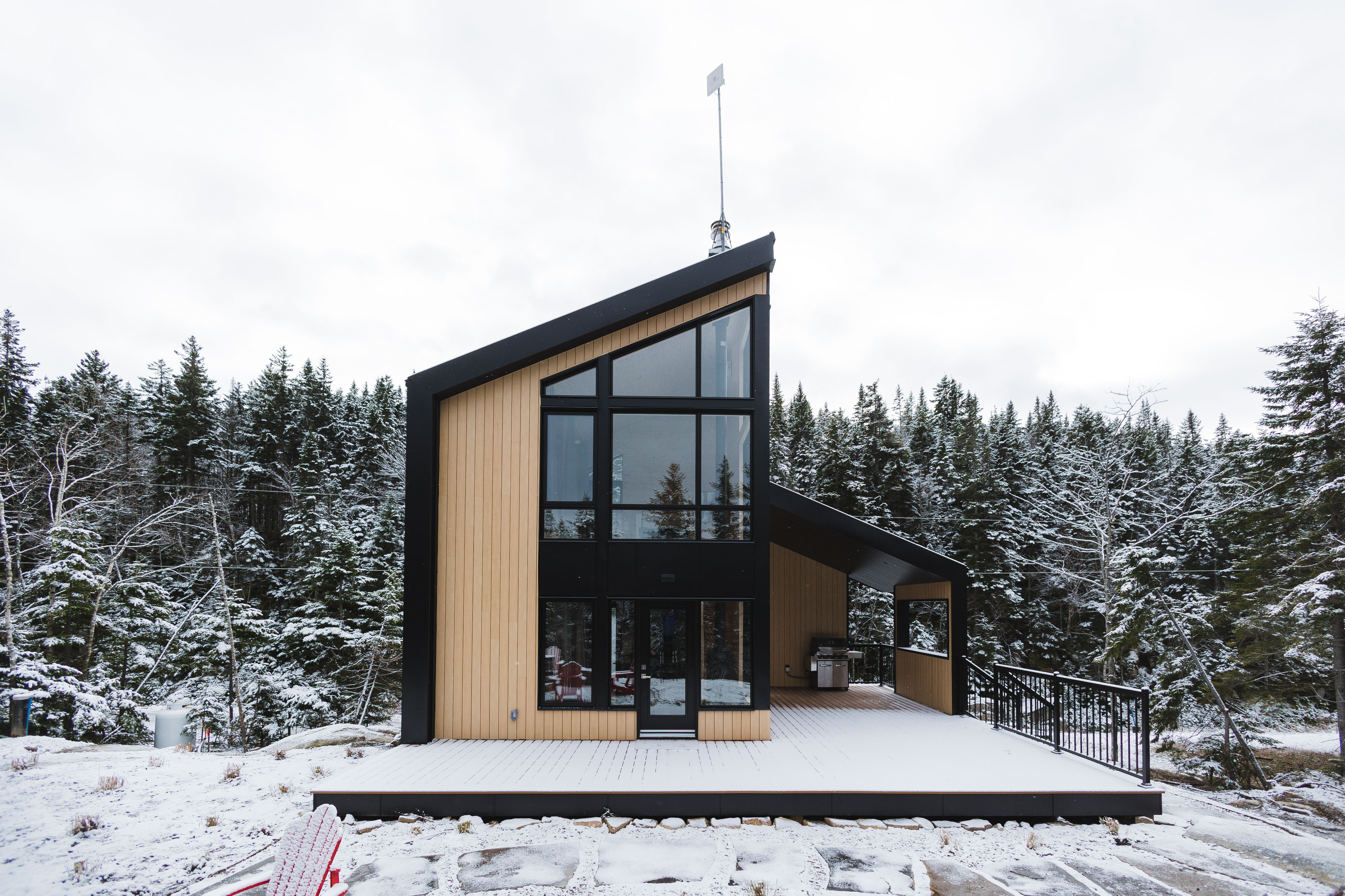 A tiny home with a deck surrounded by forestry in snow.