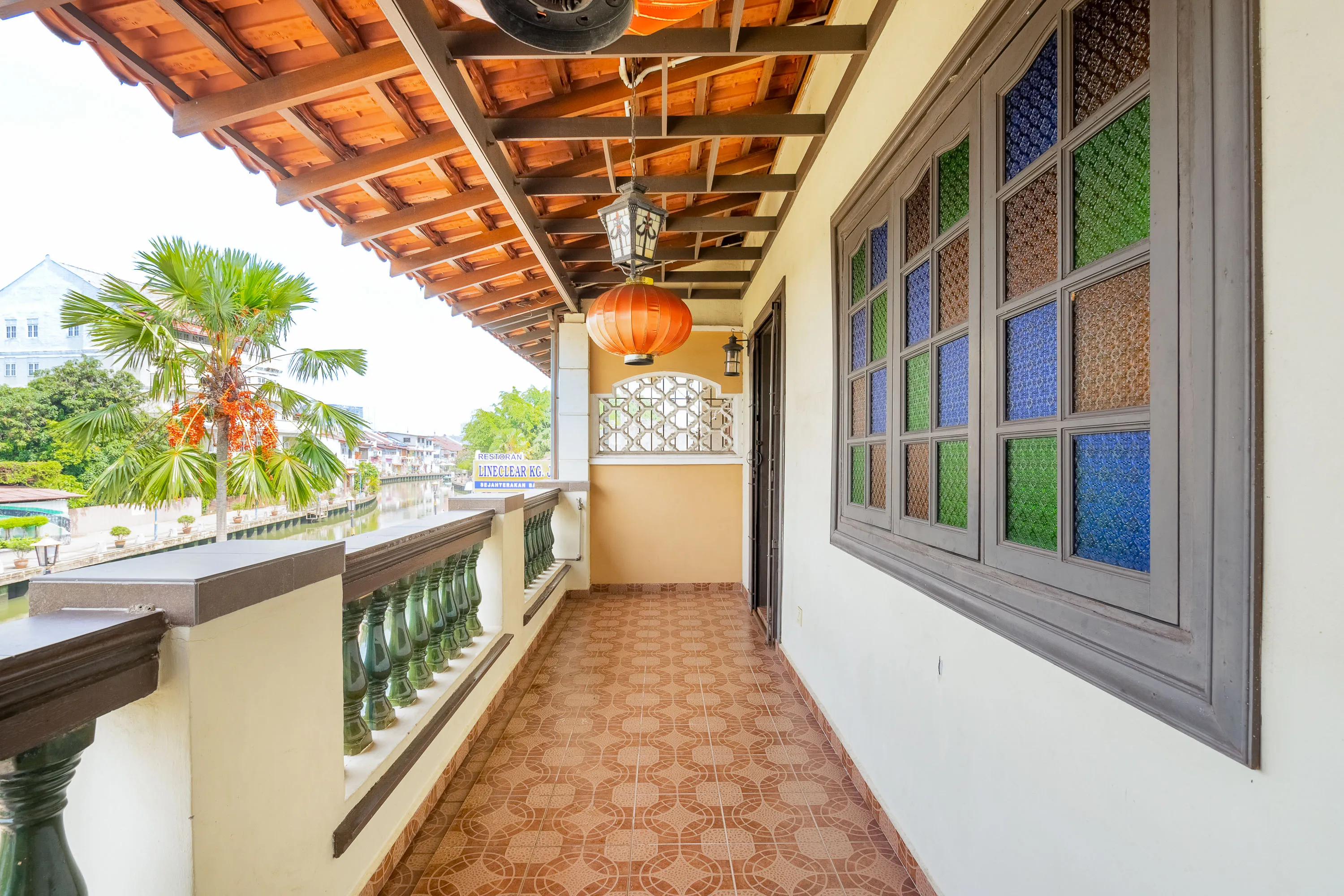 Bright and long outdoor patio with tile floor and colorful stain glass windows, flanked by palm trees.