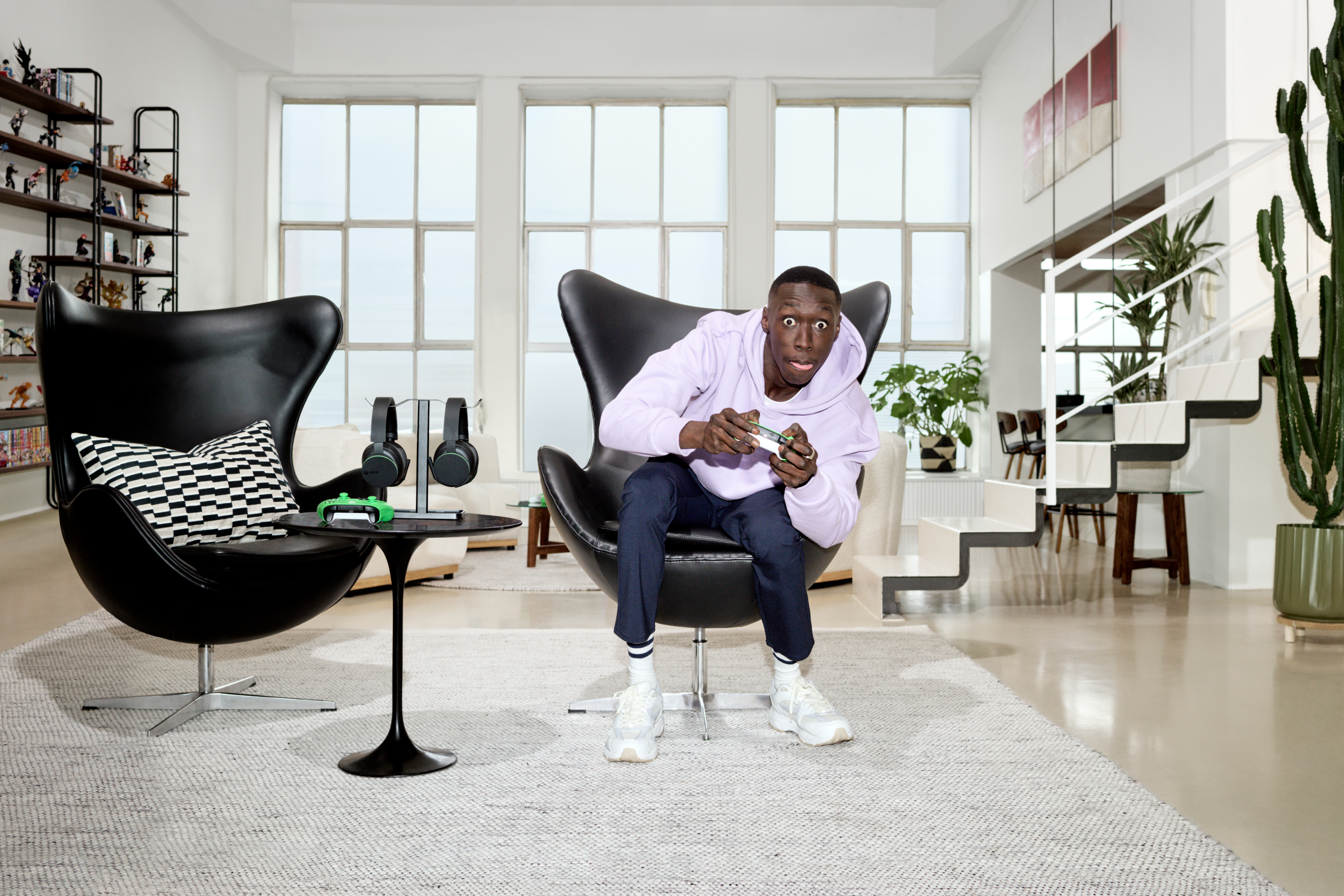 Man enthusiastically playing a video game sitting in a black chair in a modern, mostly black and white living room. 