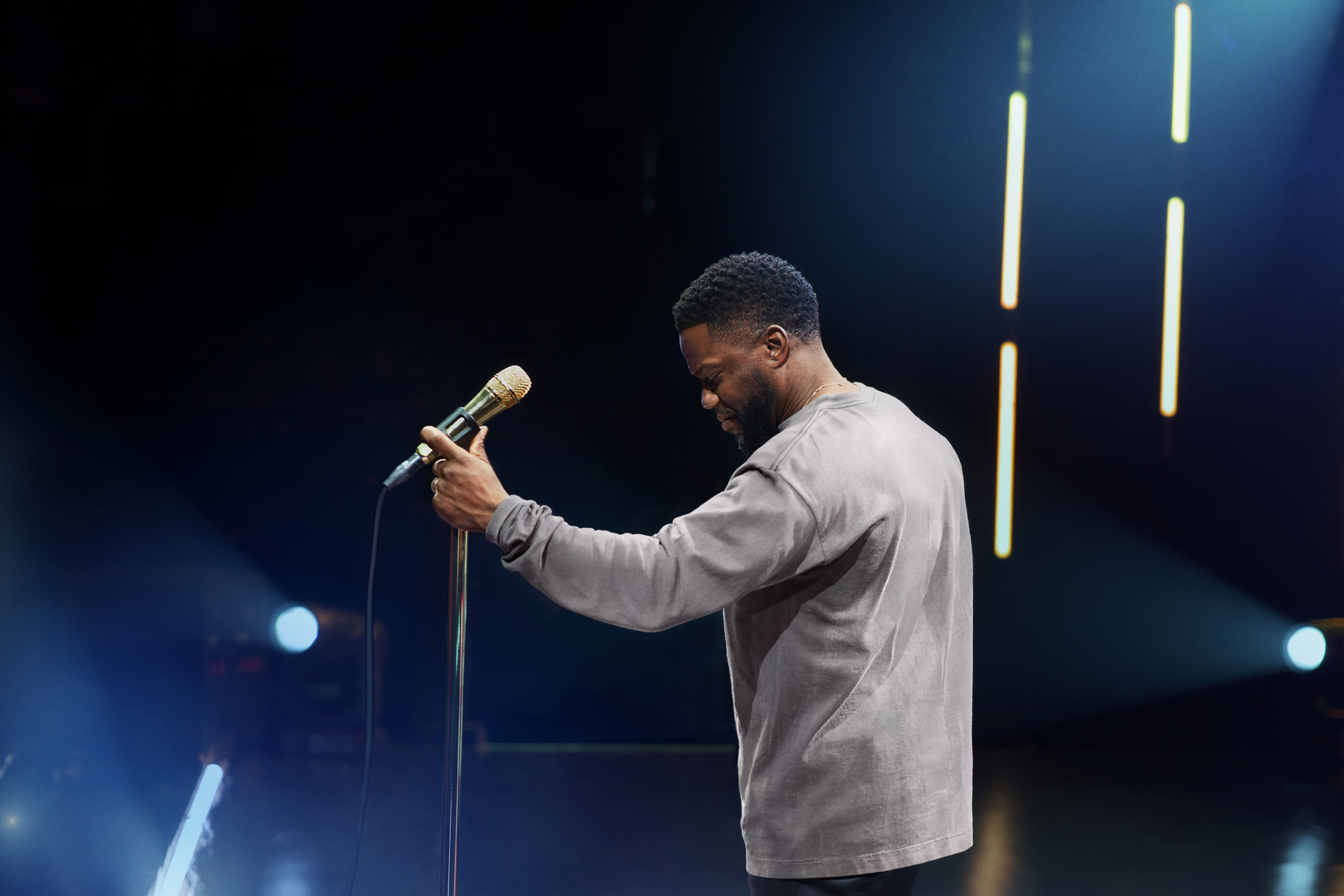 Stage performer in a grey shirt, adjusting a microphone on stage.