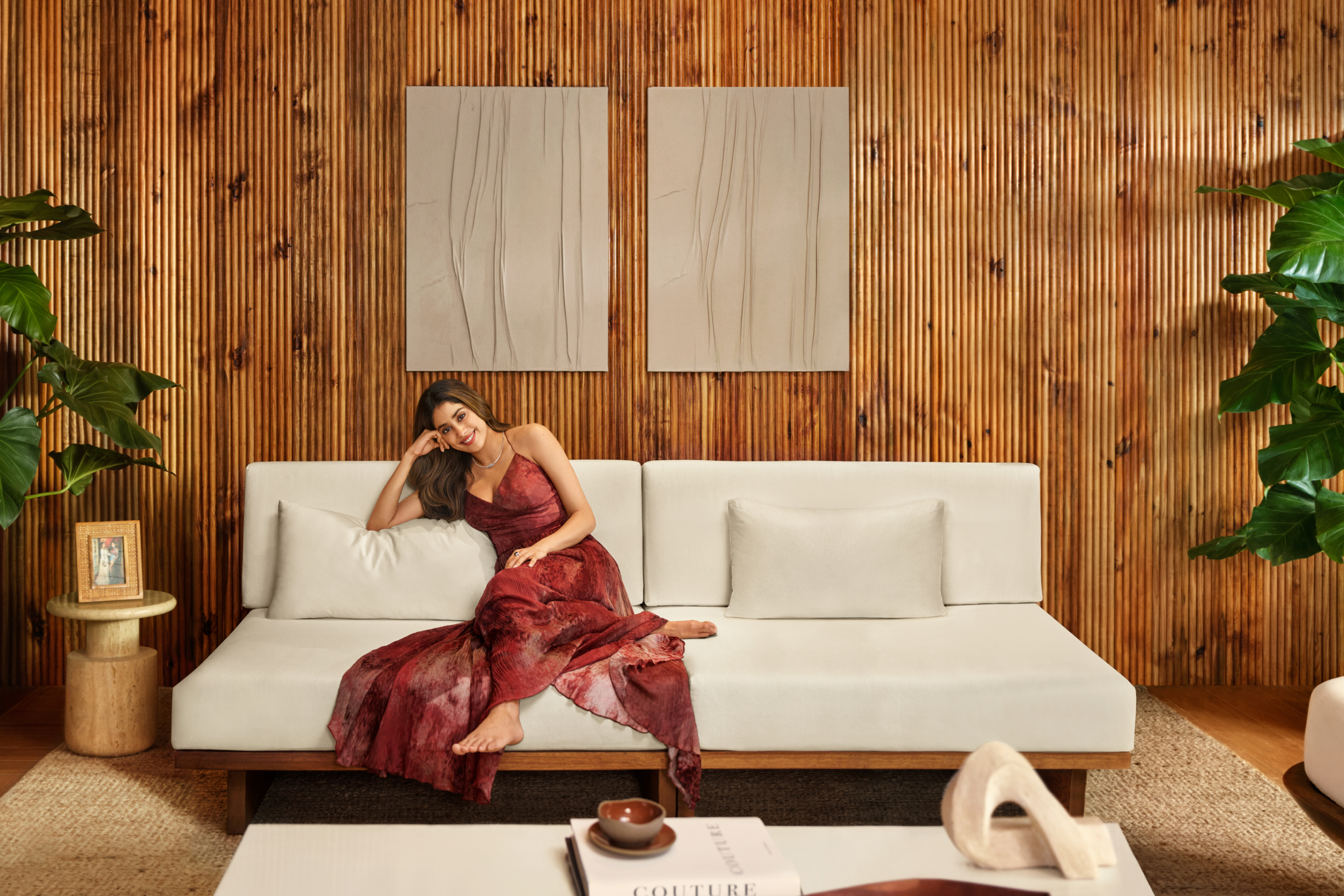 Woman in a red dress smiling and sitting on a white couch against a wood paneled wall. 