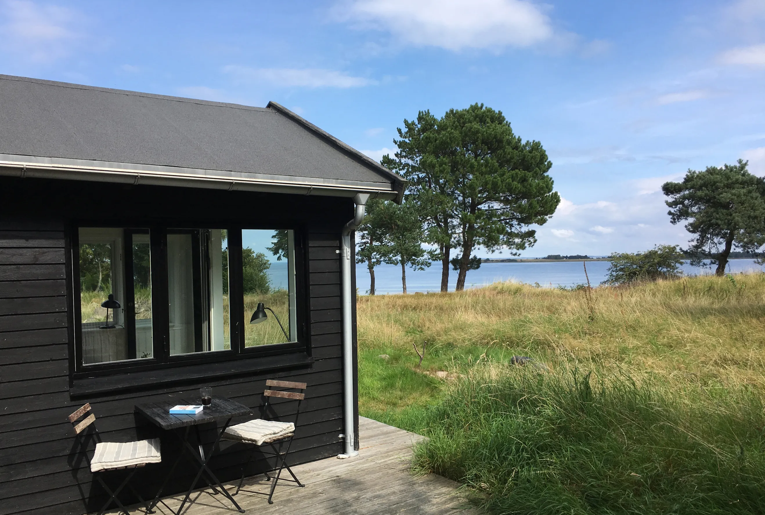 Exterior shot of a summerhouse in Denmark, showing garden furnture in the foreground and the seashore in the background.