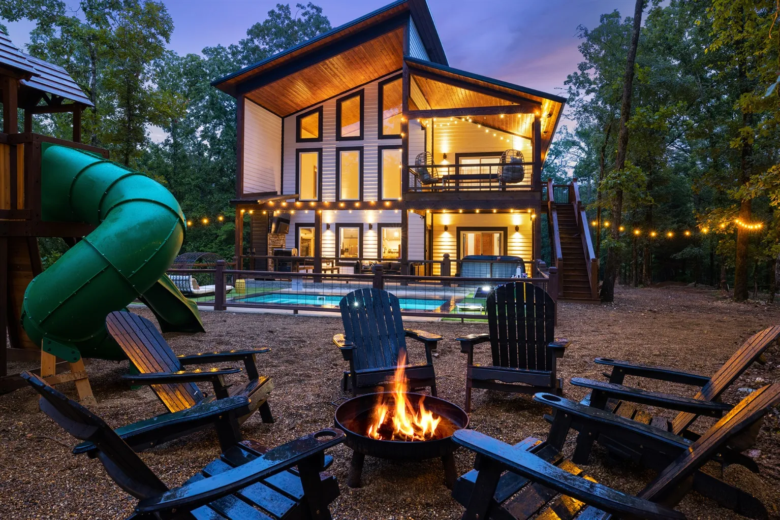 Exterior shot of a modern three story cabin set in woodland. Fire pit and childrens' slide in the foreground.