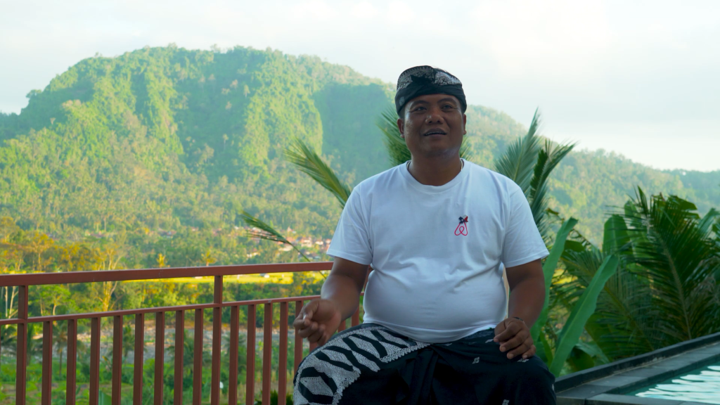 Man with white shirt sits in front of a green, mountainous backdrop