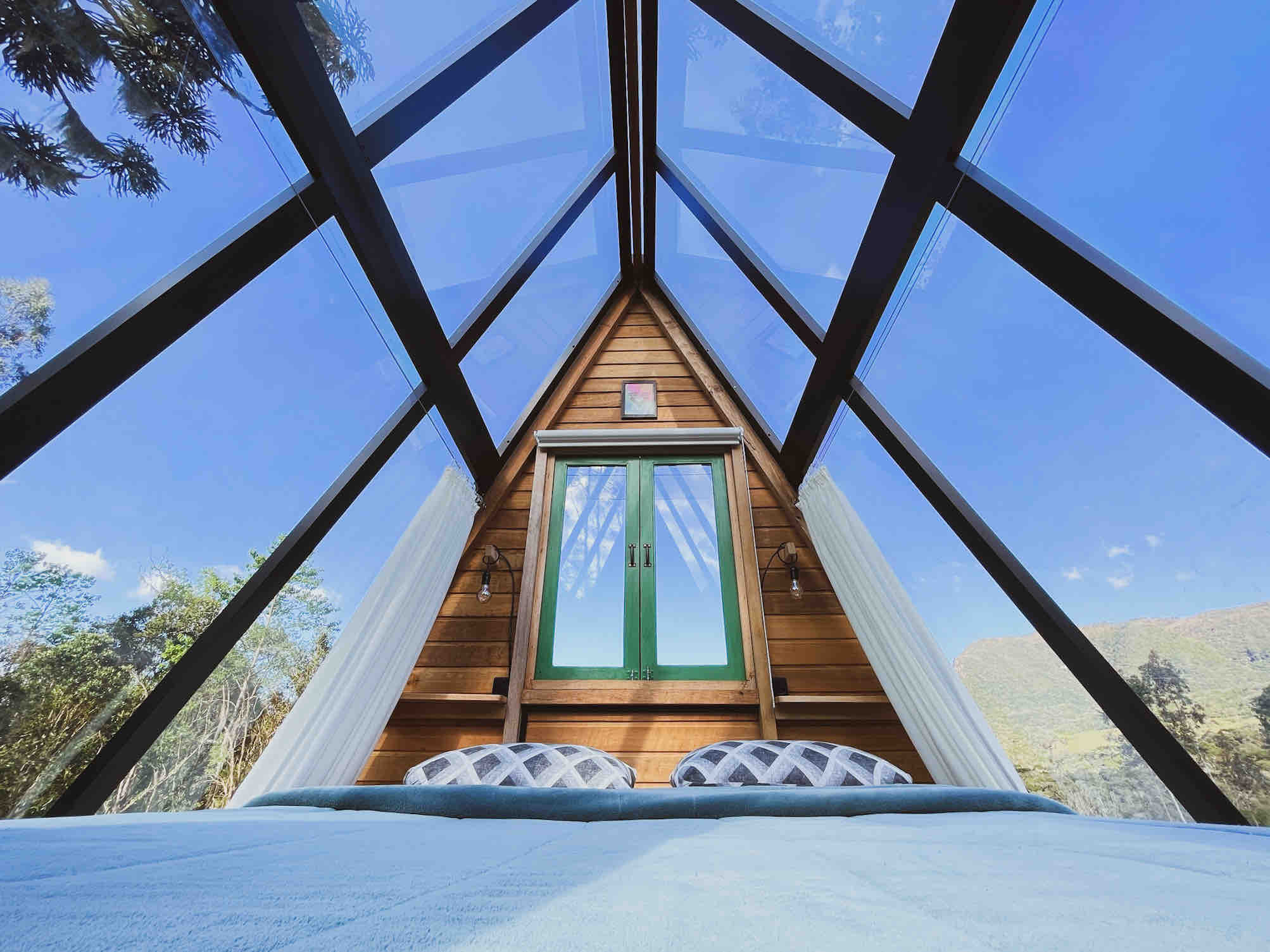 View of the bed inside of a glass pyramid with the blue sky in the top