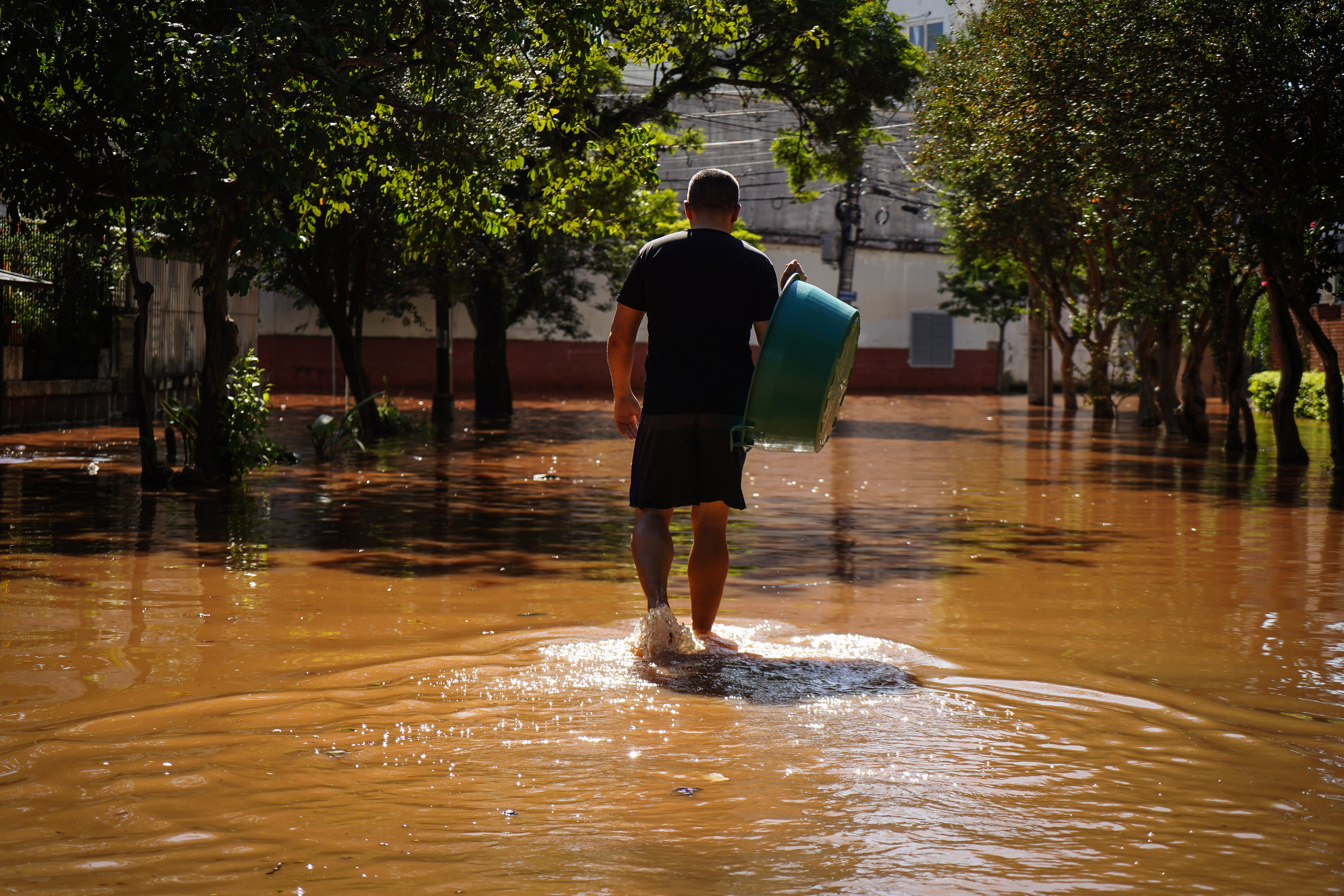 Man walks through floodwaters holding a plastic tub
