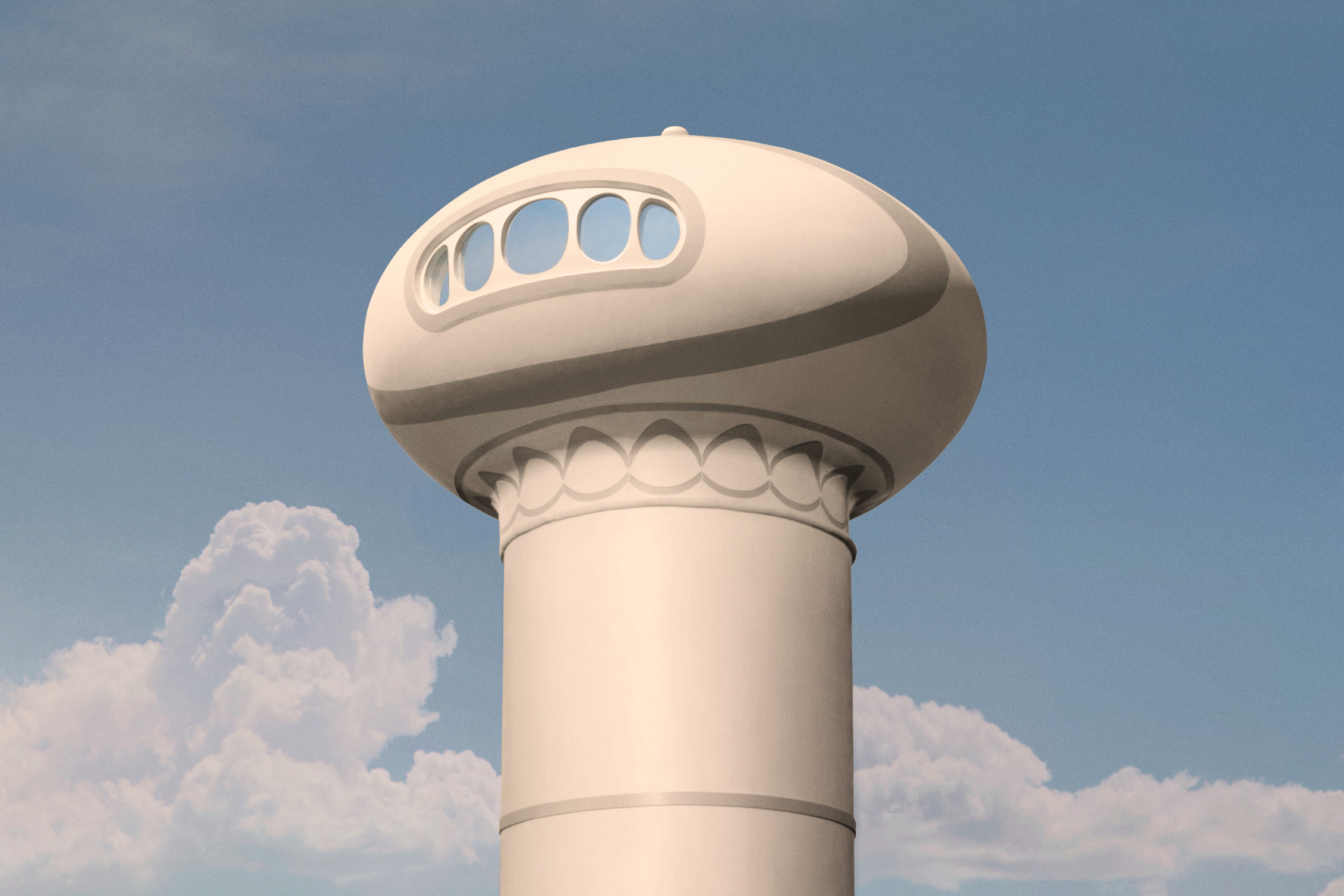 An outisde view of a control center tower with 5 circular windows set against a blue sky with white fluffy clouds.