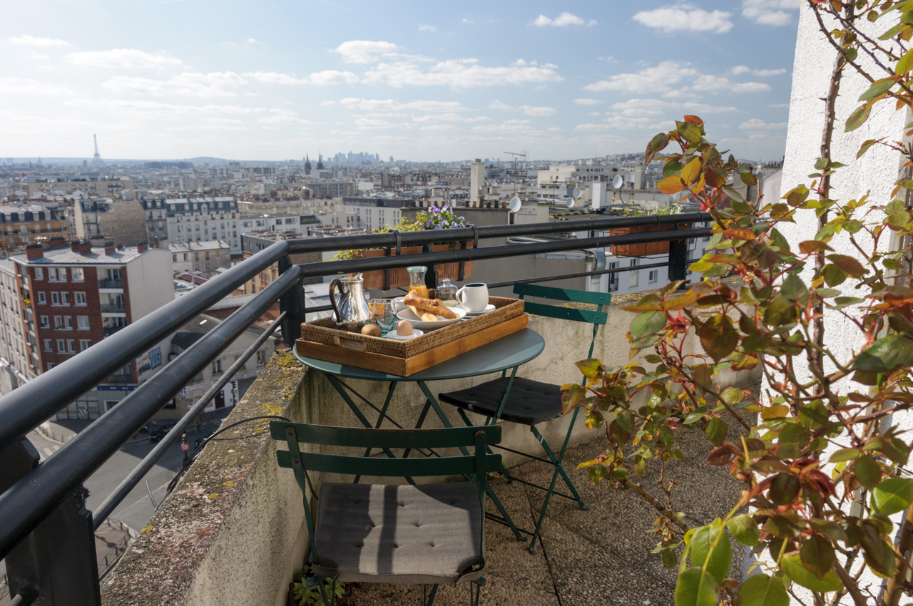 Balcony with two chairs and a table set for breakfast, with views of the Paris skyline and the Eiffel Tower in the background.