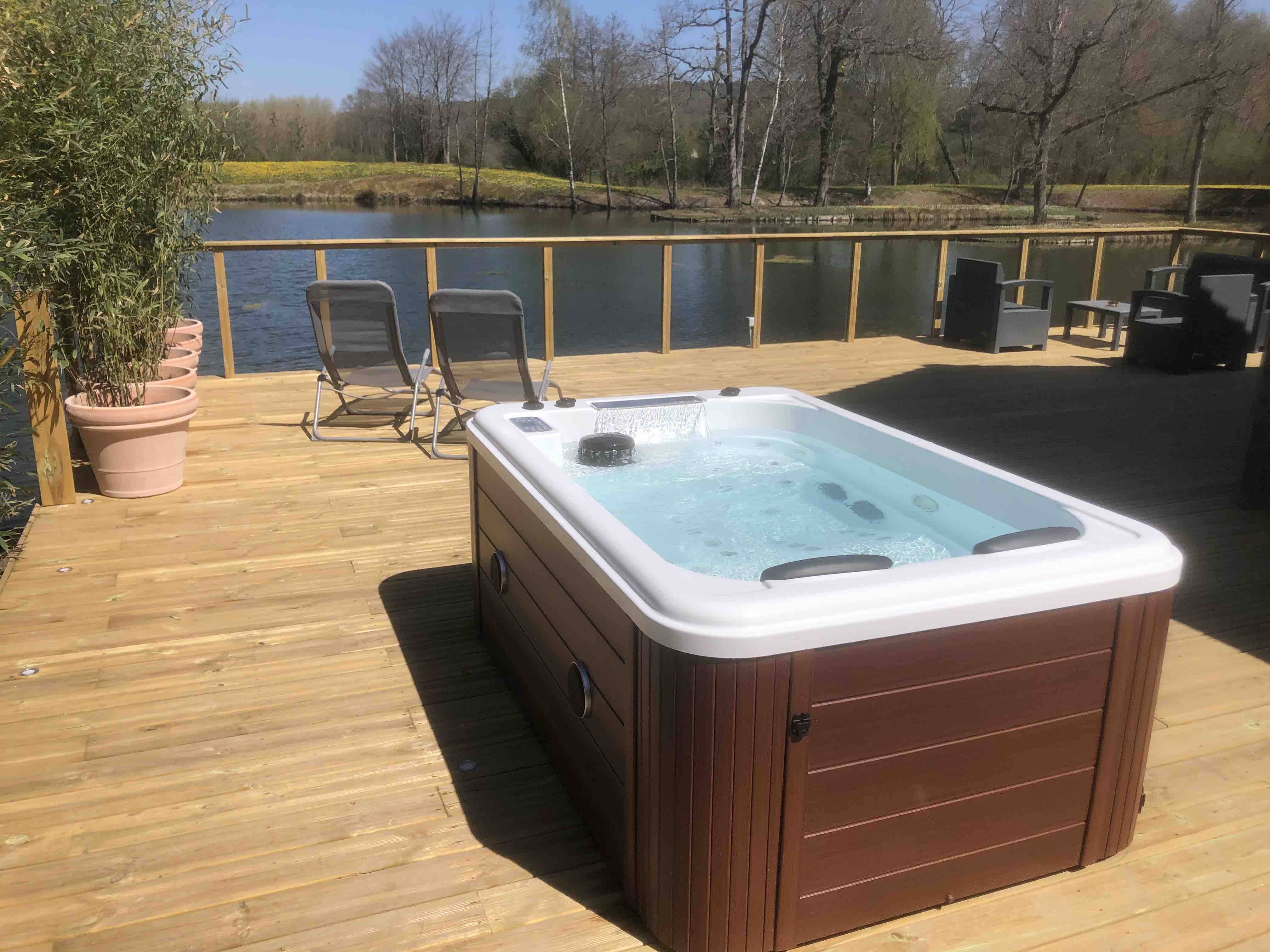 Exterior shot of a jacuzzi on timber decking overlooking a small pond and woodland.