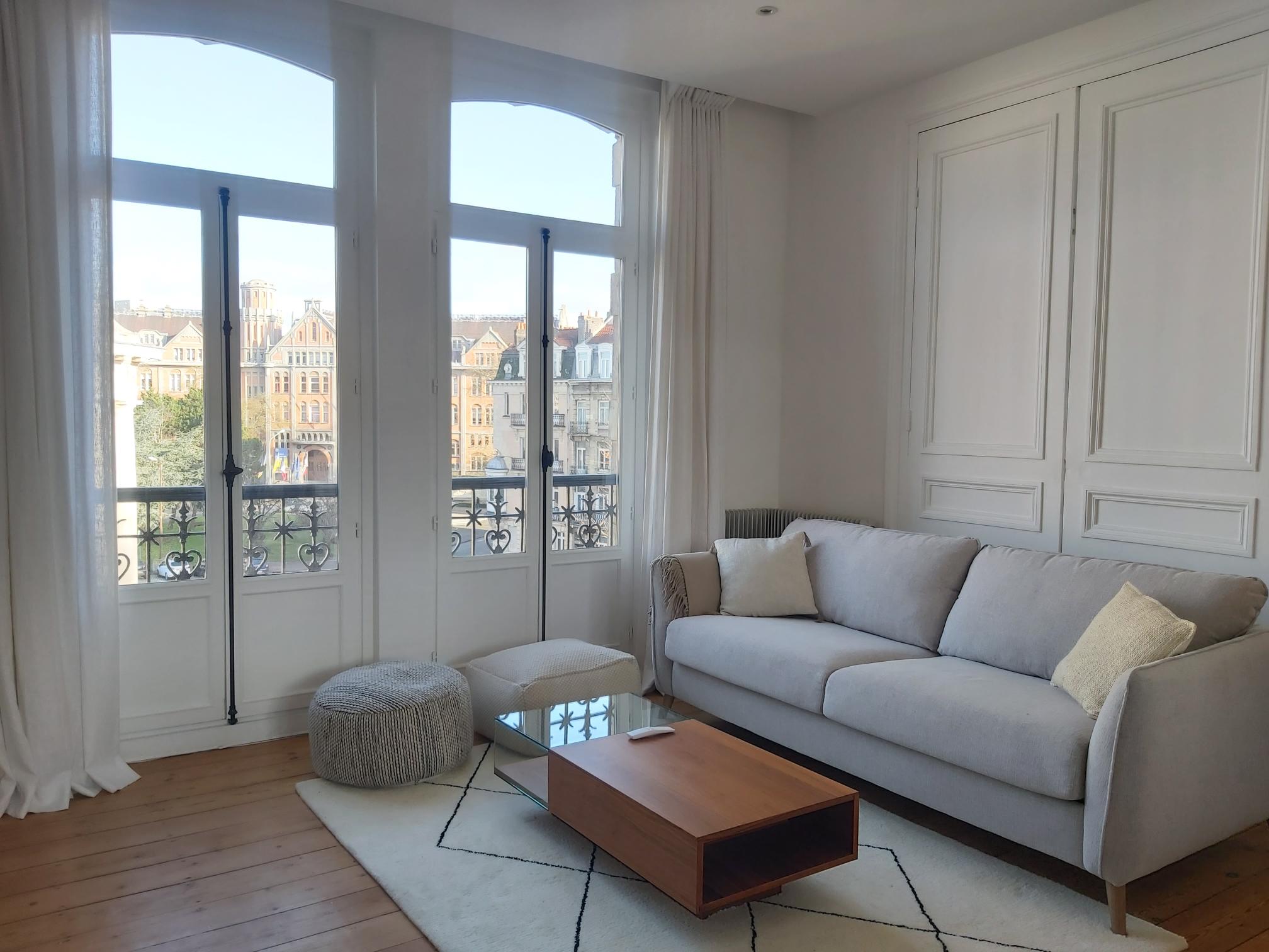Interior shot of a stylish living room in an old apartment in Little. Balcony doors offer a glimpse of the historic city centre outside.