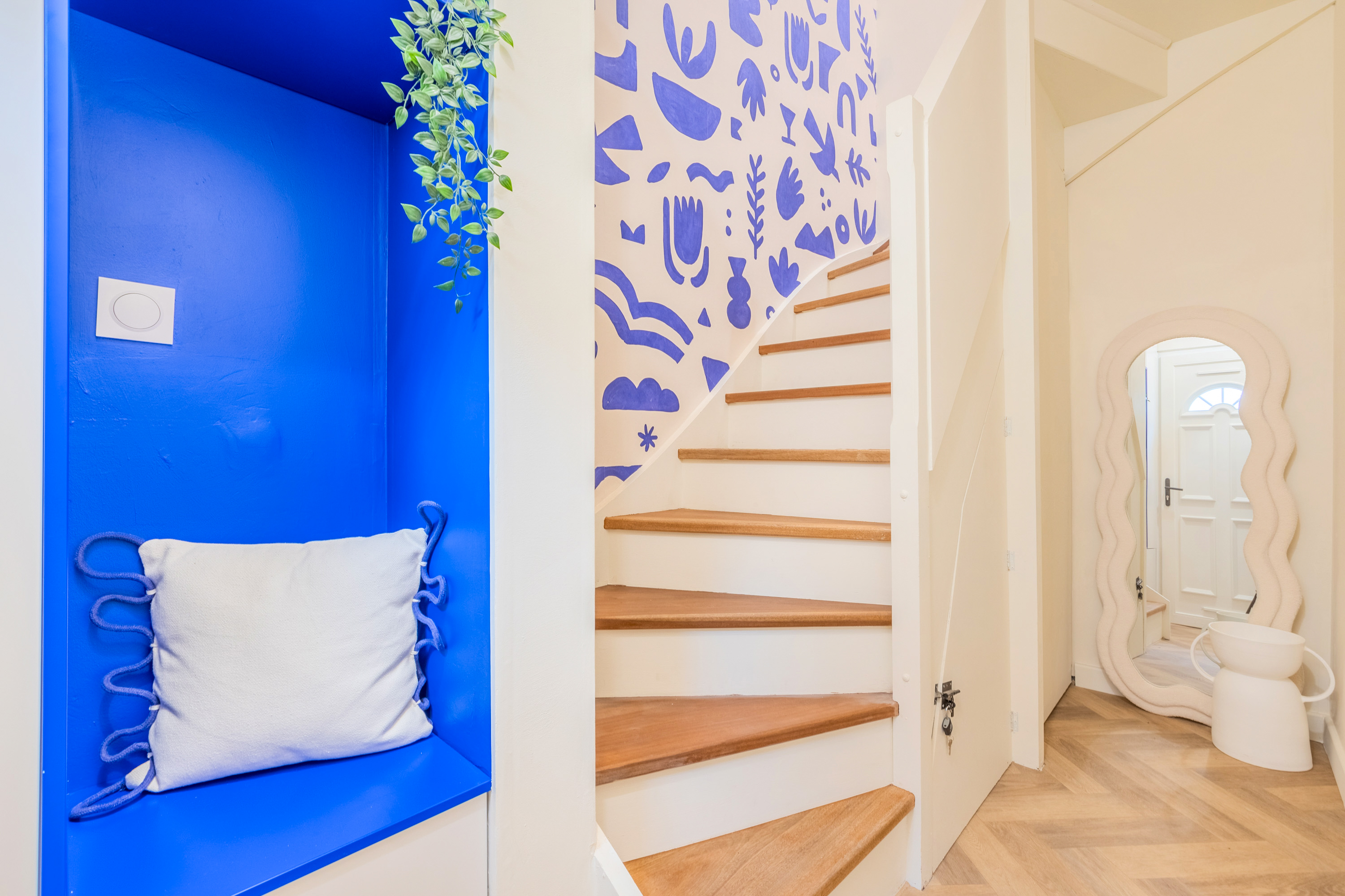 Interior shot of a duplex studio apartment in Lille: showing bright blue patterned wallpaper and an exposed timber staircase.