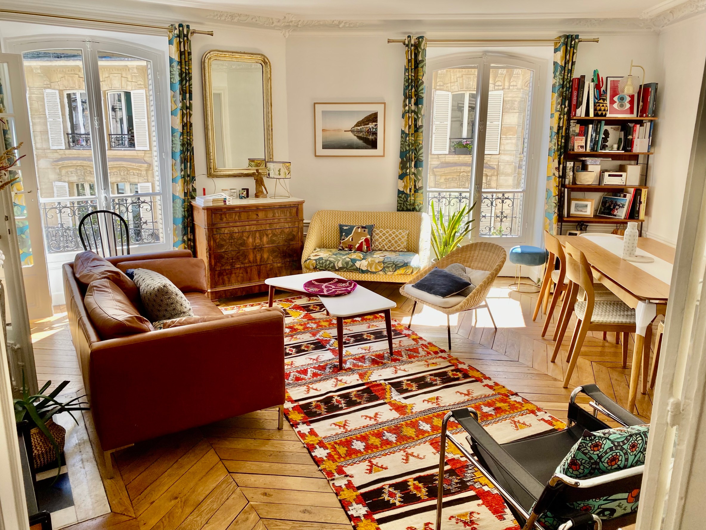Chic flat in the SoPi district of Paris. View is of a colorful living room, with parquet flooring, a kilim-style rug and an eclectic mix of antique and vintage furniture.