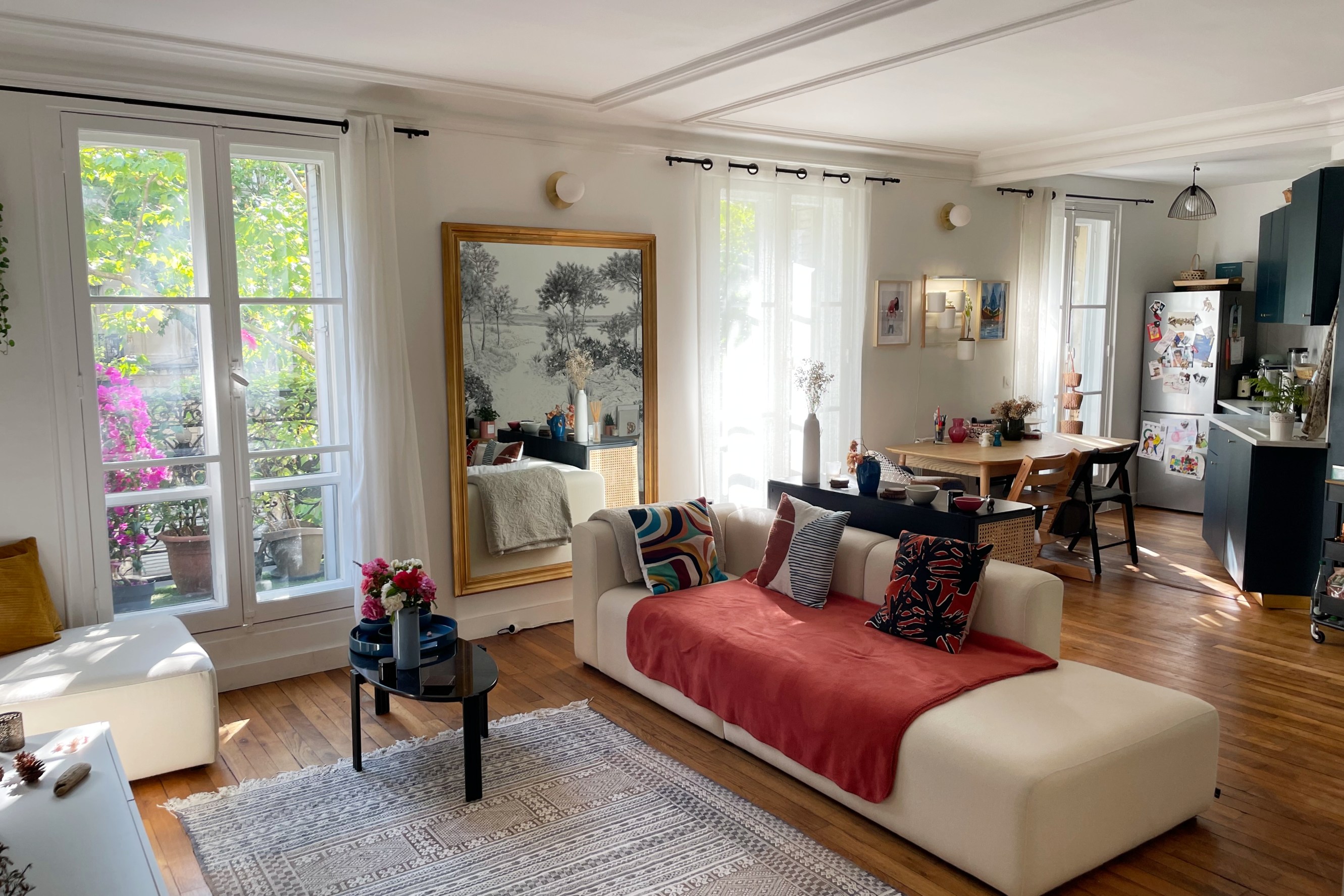 Designer Cocoon in the Porte de Clignancourt neighborhood of Paris. View of a living/ kitchen space, featuring a chaise-style sofa and light streaming in from three traditional french windows.