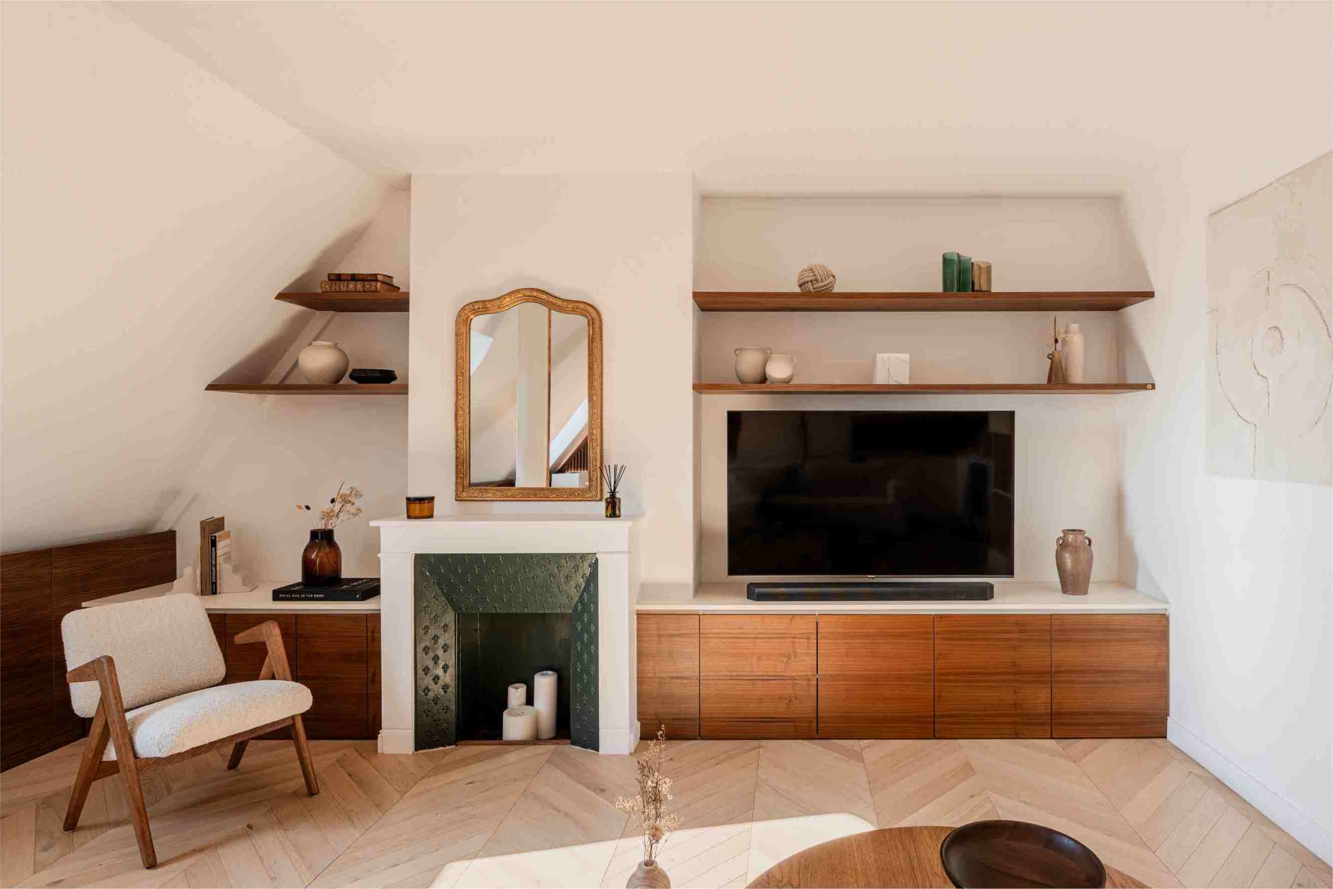 Designer apartment at the Champs-Élysées in Paris. View is of a stylish living room, built under the eaves, featuring a built-in credenza, a fireplace and a mid century modern armchair.