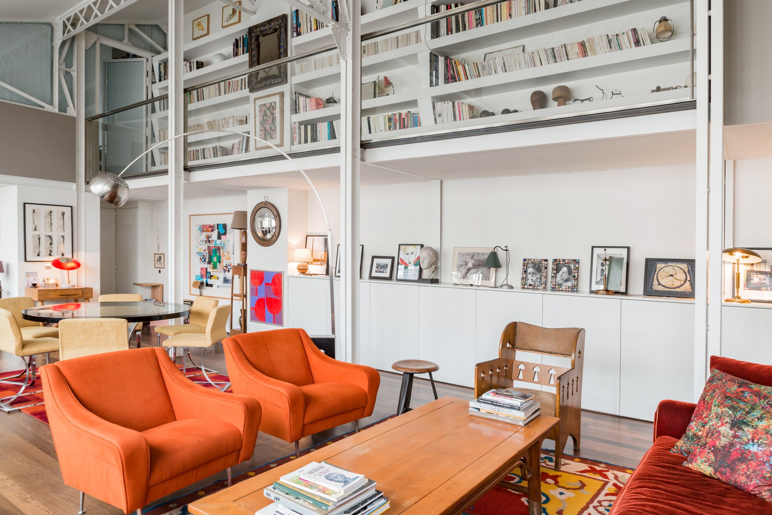 Industrial loft in Le Marais. View of a high ceiling living/ dining space, featuring organe armchairs and a large designer floor lamp
