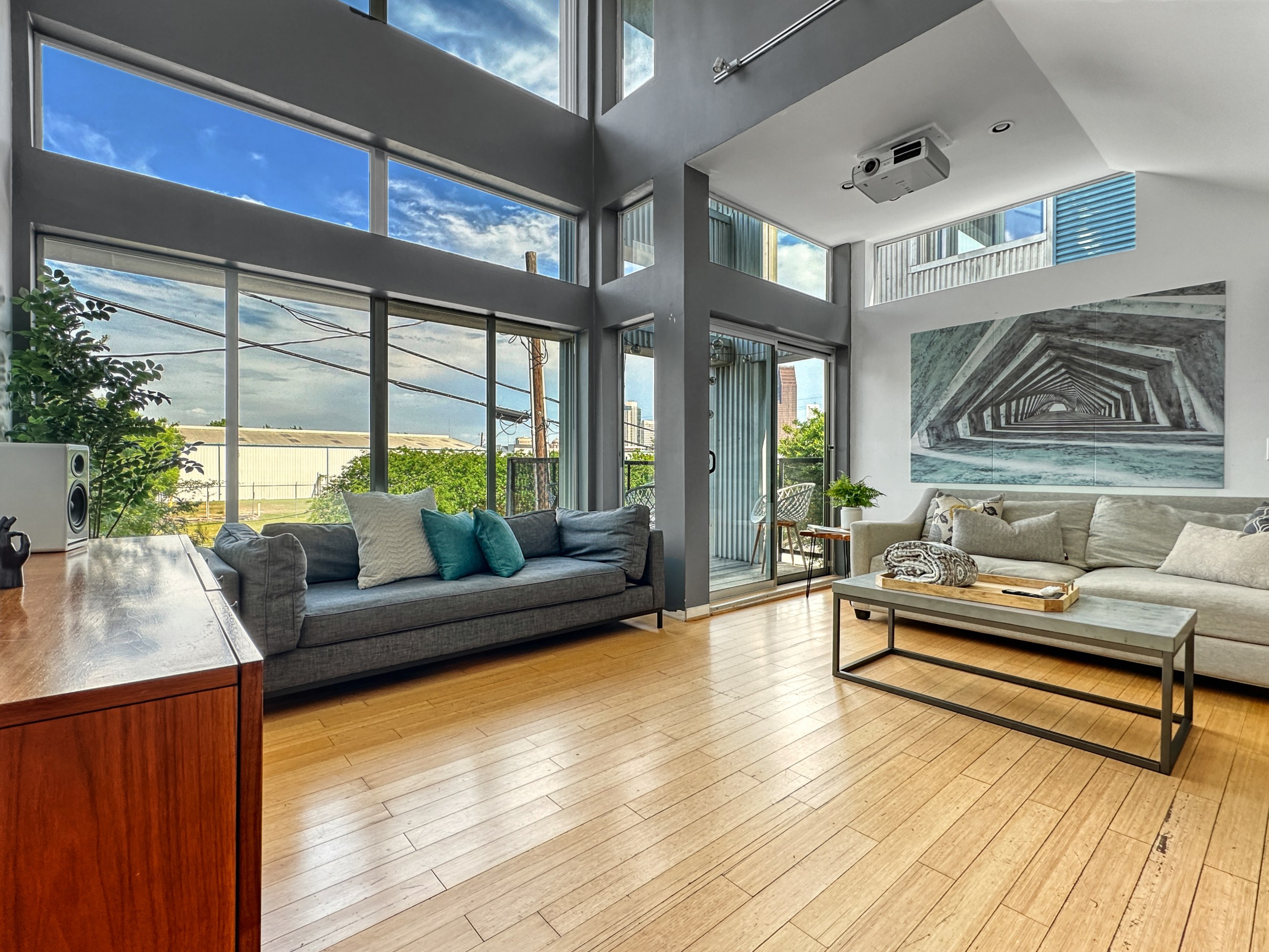 Room with a wooden floor and gray couch in front of a panel of windows